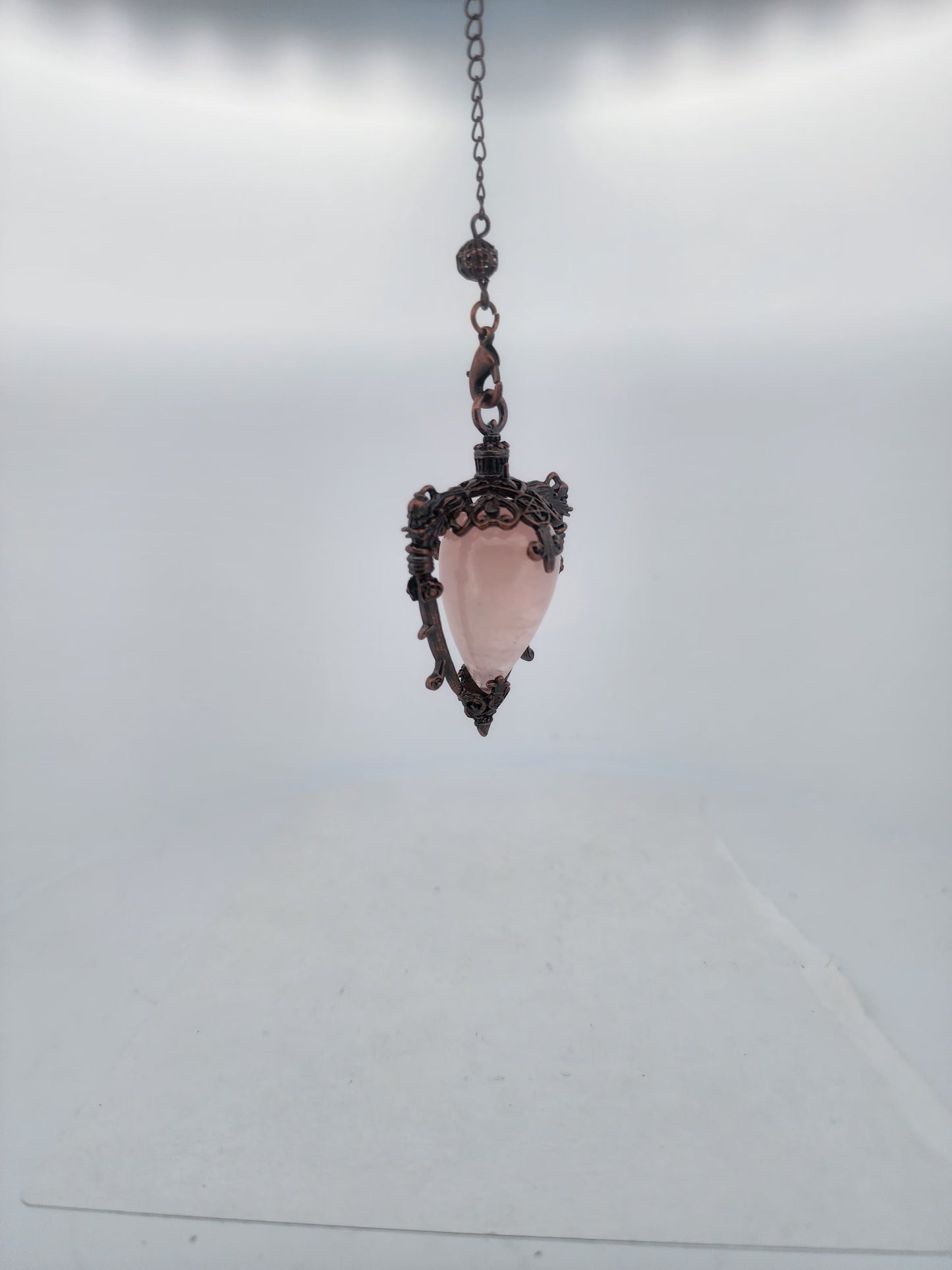 Pink crystal pendant with decorative metal frame on a chain against a light gray background