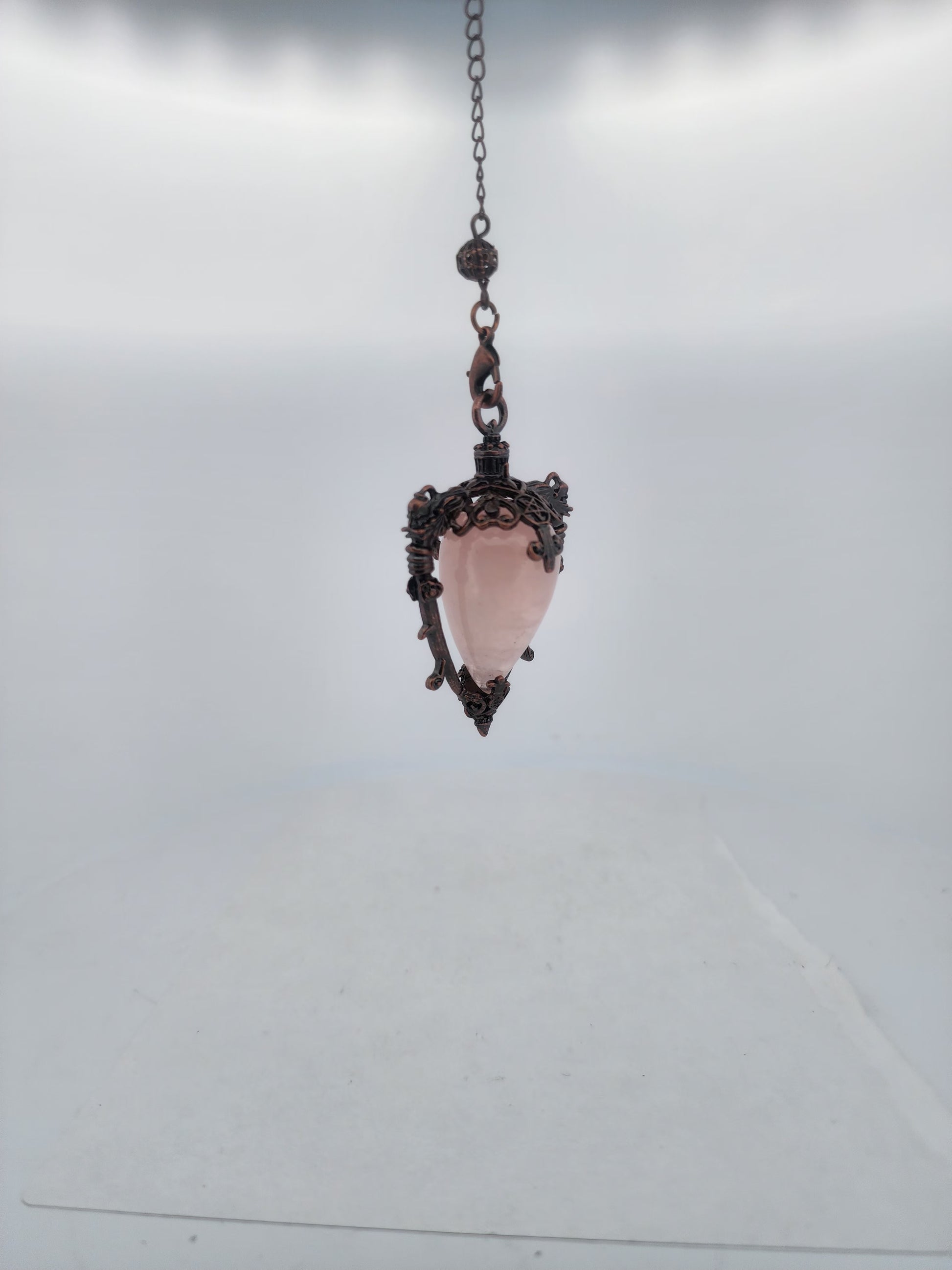 Pink crystal pendant with decorative metal frame on a chain against a light gray background