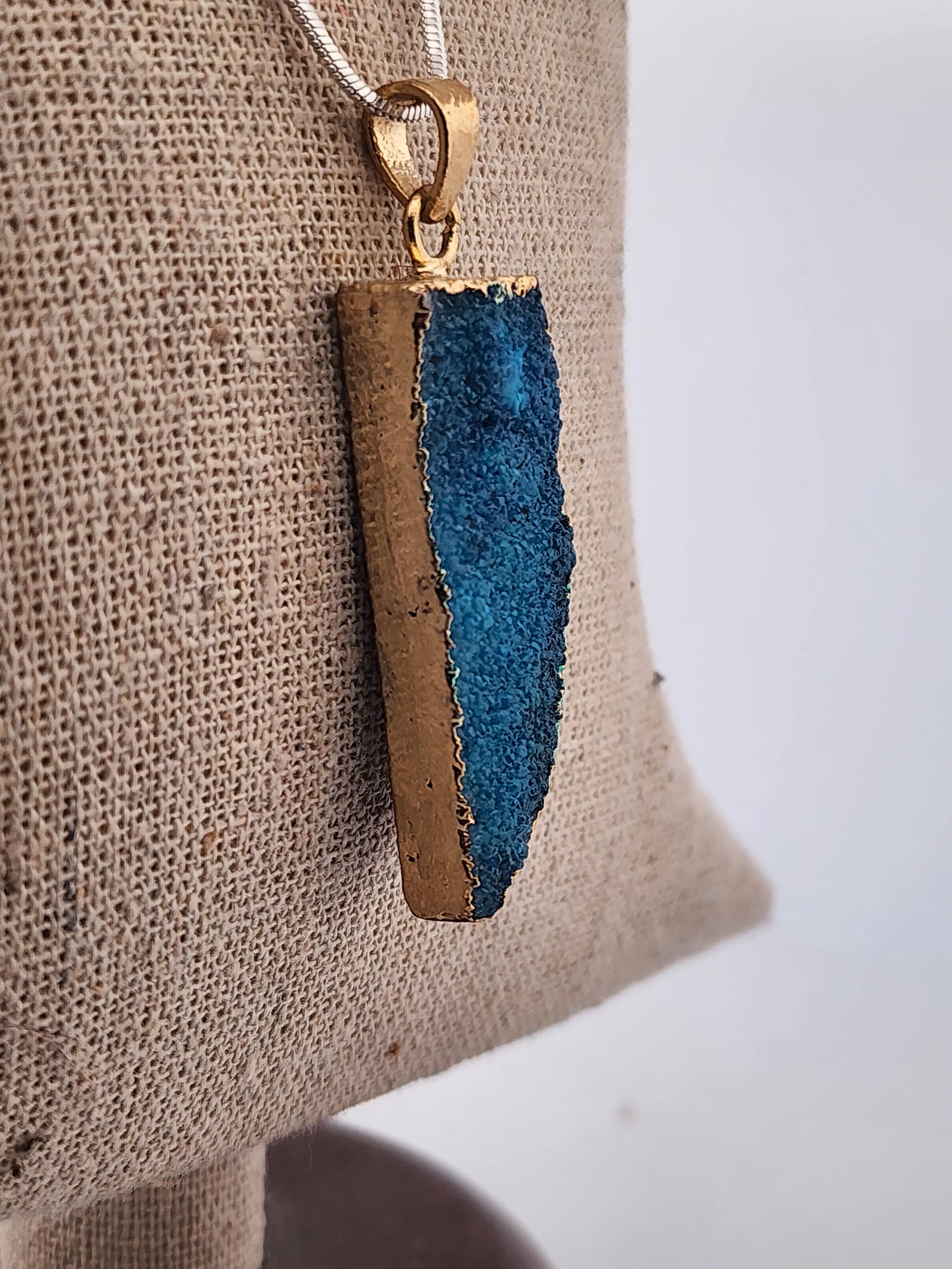 Jewelry pendant with blue and gold design on a beige fabric background