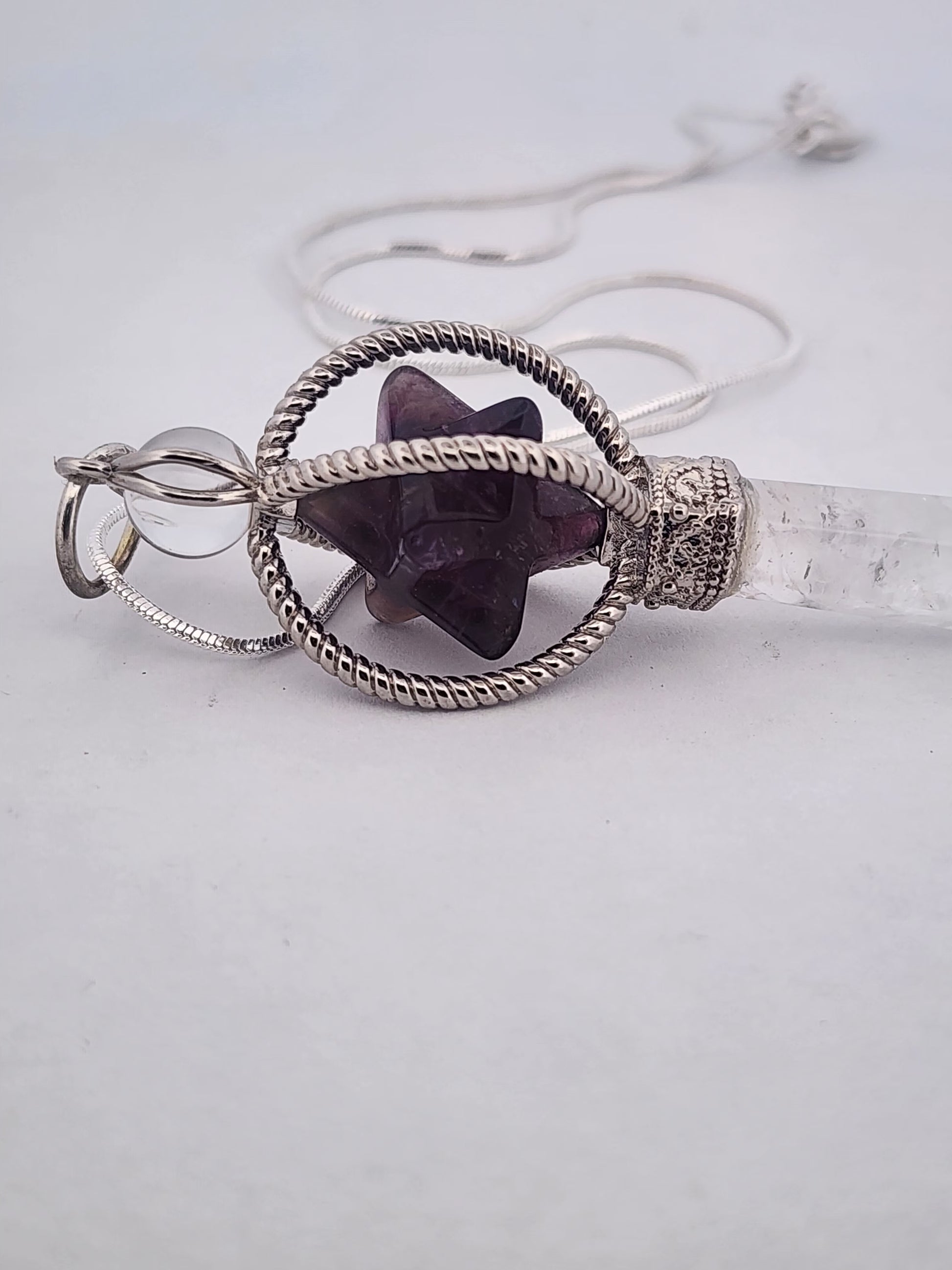 Crystal necklace with purple stone and silver wirework on a light gray background