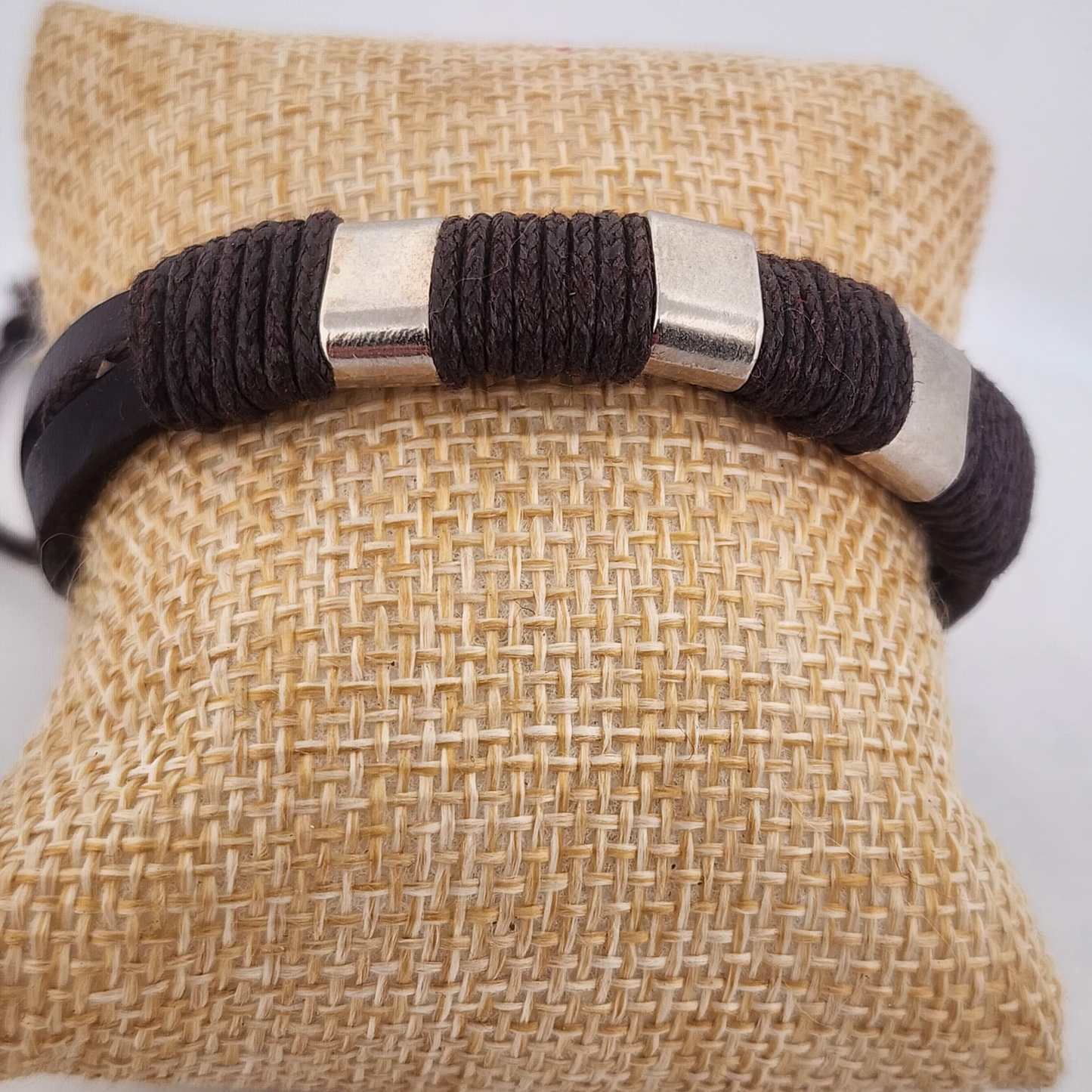 Bracelet with brown cord and silver accents on a textured beige pillow
