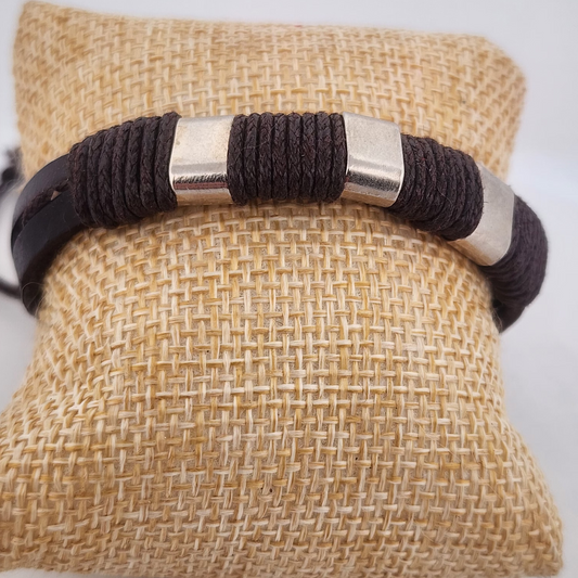 Bracelet with brown cord and silver accents on a textured beige pillow