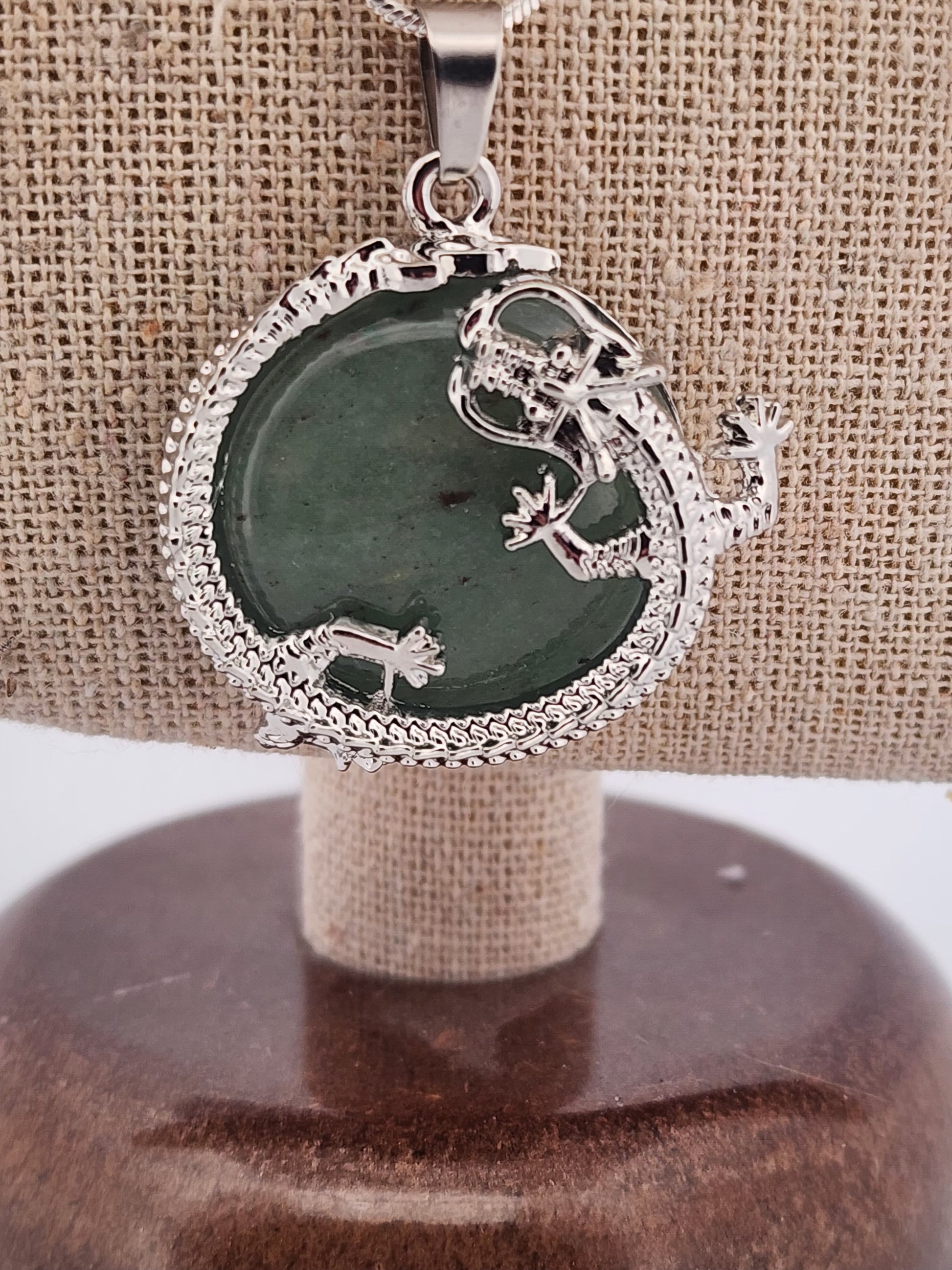 Silver pendant with green stone on a wooden stand against a beige fabric background