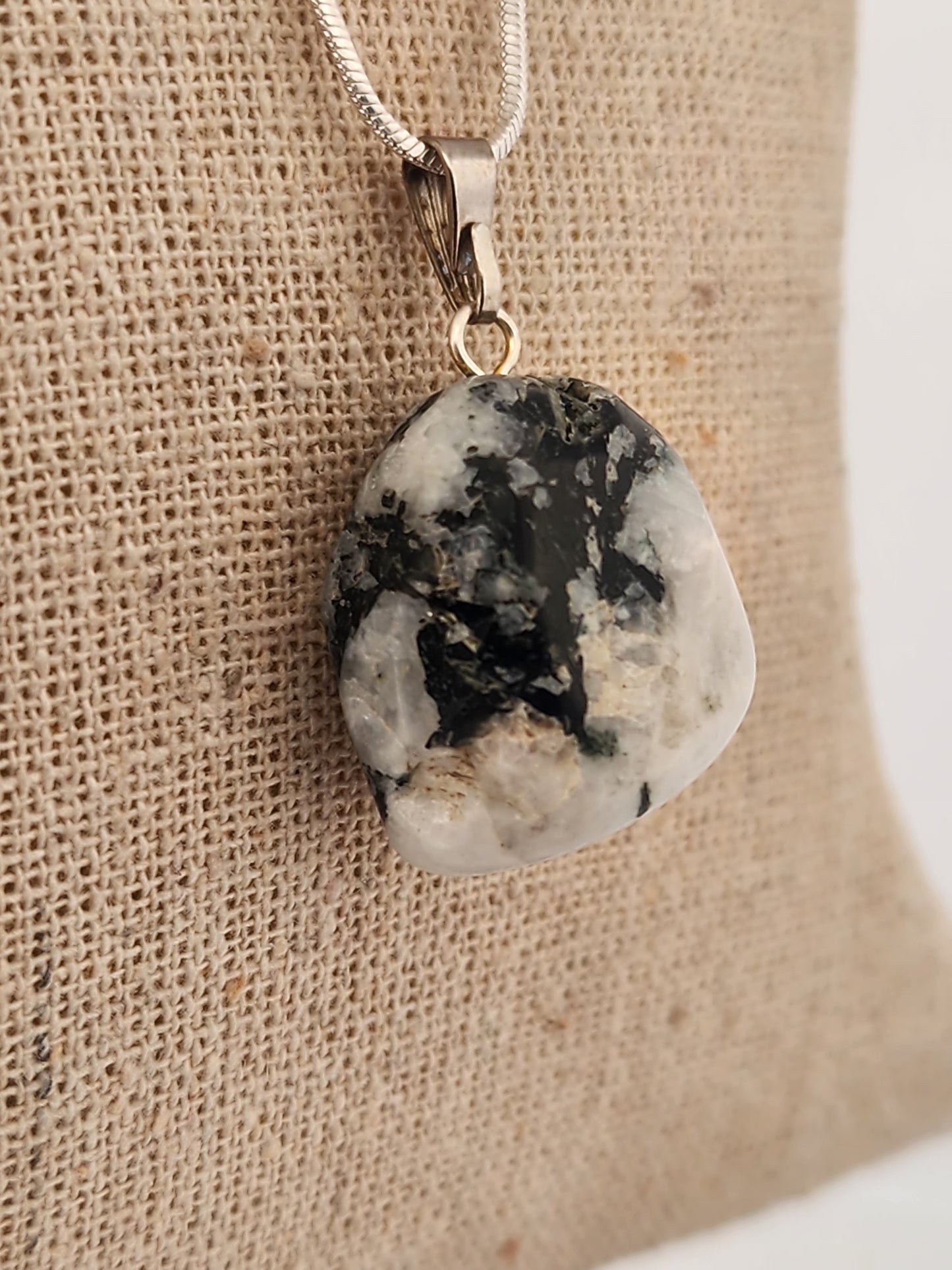 Necklace with a pendant featuring a black and white stone on a beige fabric background
