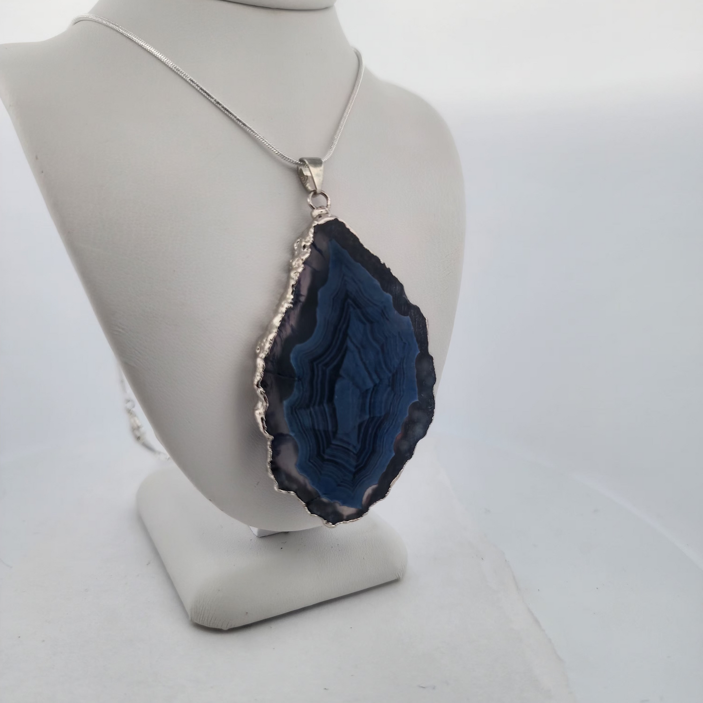 Blue geode pendant on a necklace displayed on a mannequin bust against a white background