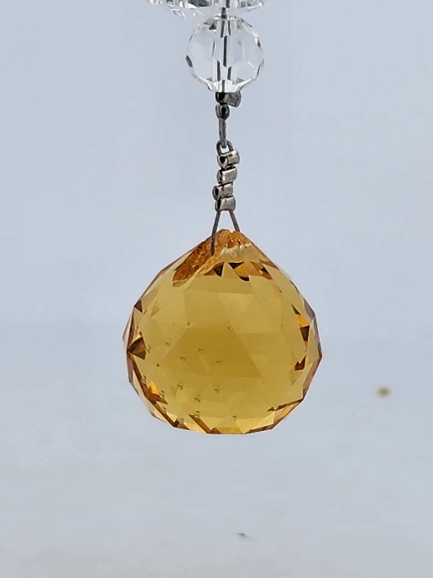 Yellow faceted crystal hanging against a light gray background