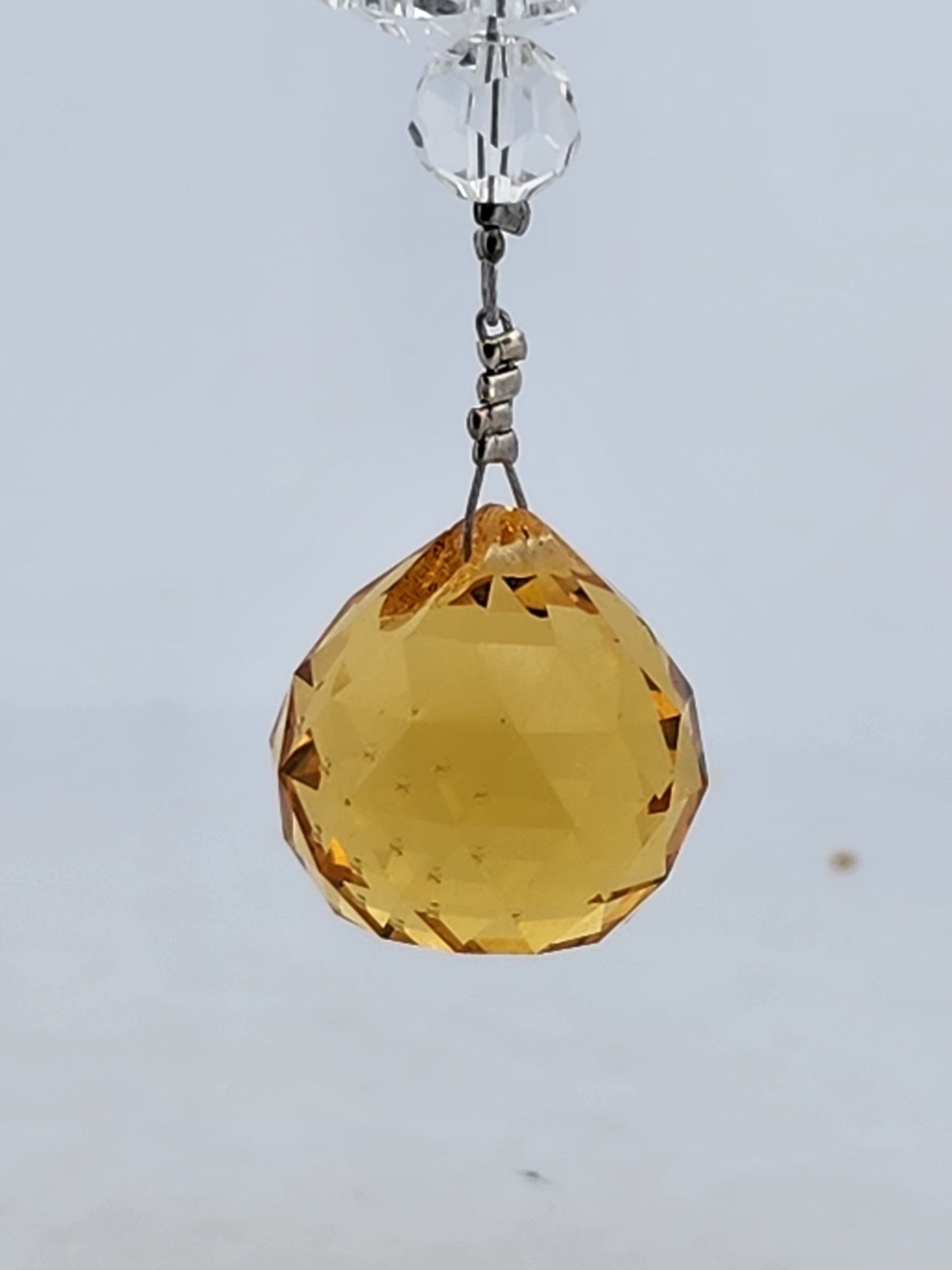 Yellow faceted crystal hanging against a light gray background