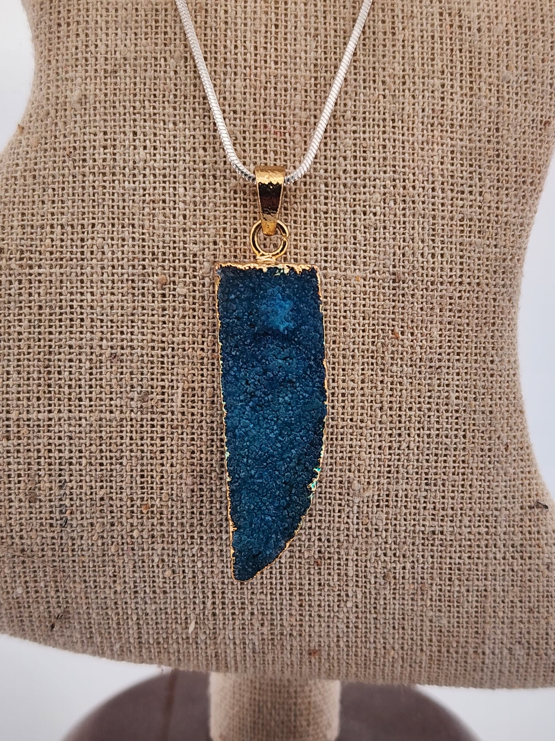 Blue druzy pendant necklace on a beige fabric background