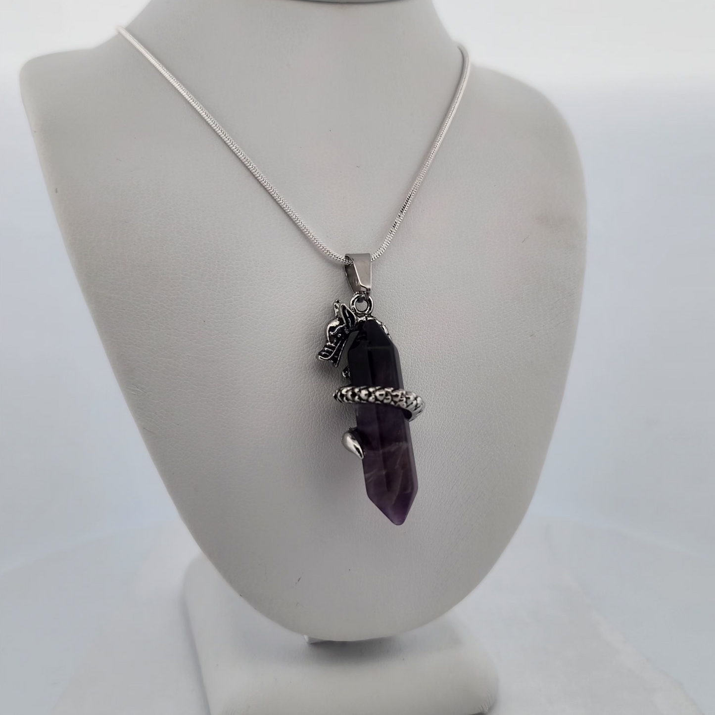 Necklace with a purple crystal pendant on a white stand