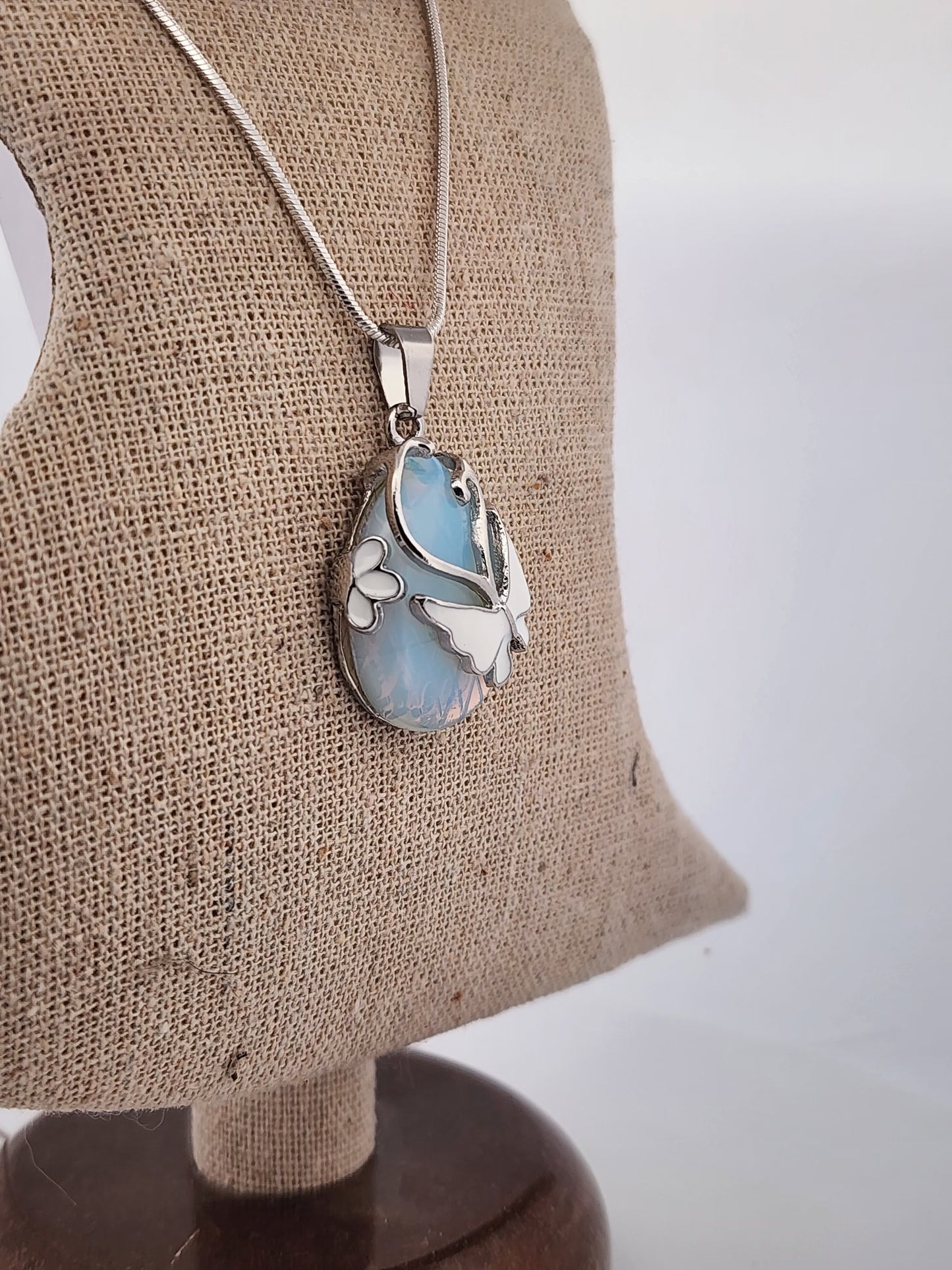 Butterfly-shaped pendant on a chain displayed on a brown fabric stand.