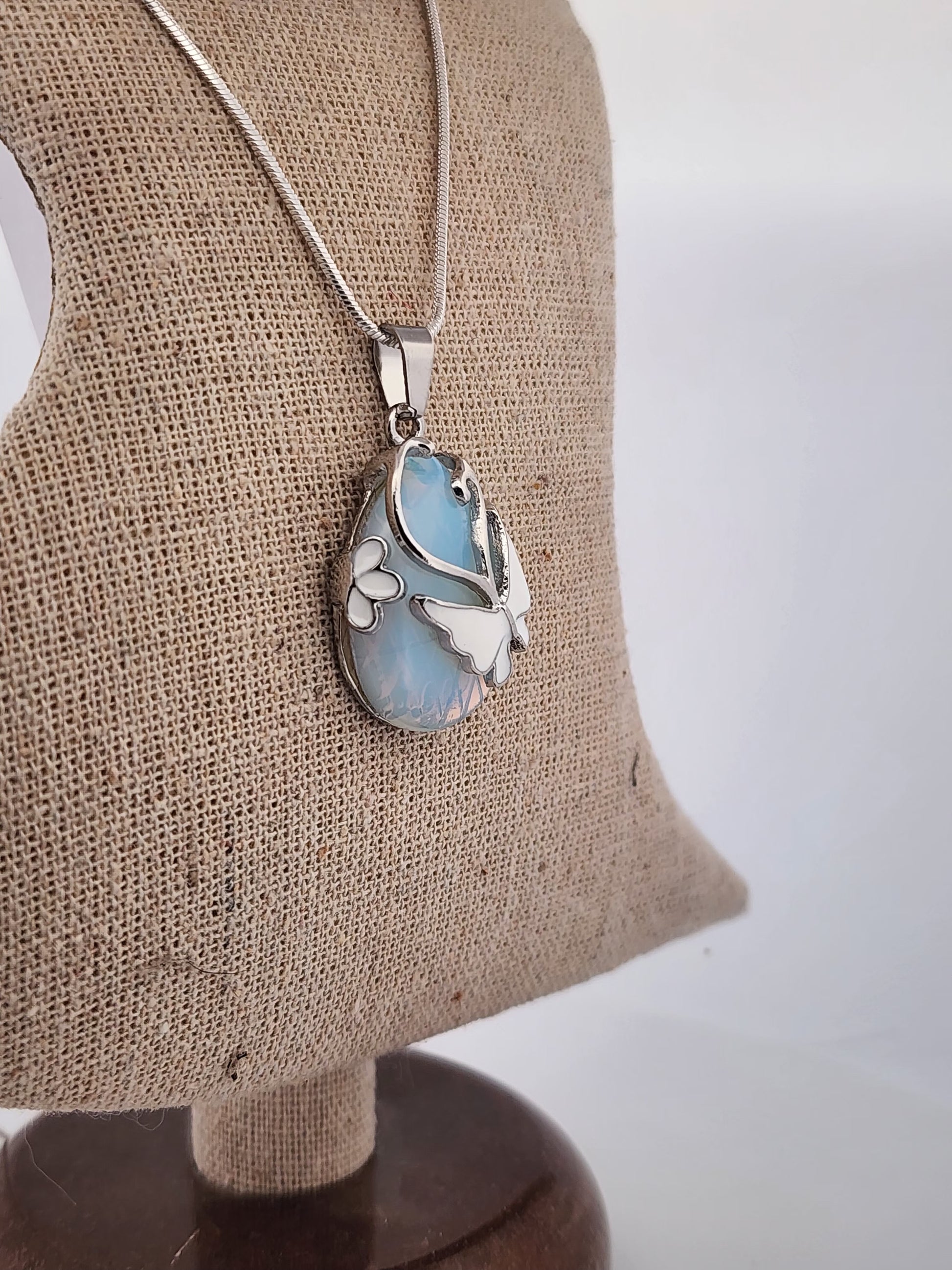 Butterfly-shaped pendant on a chain displayed on a brown fabric stand.