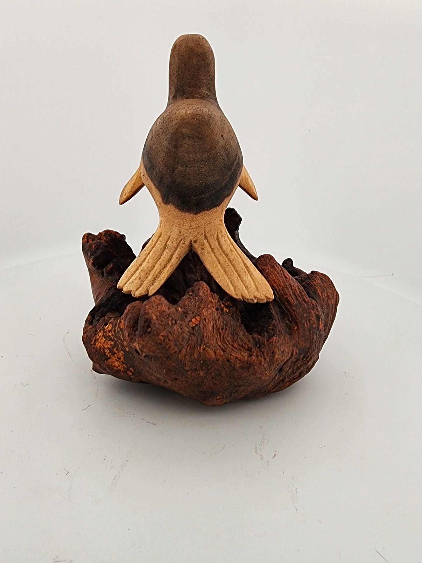 Wooden sculpture of a bird perched on a branch against a white background