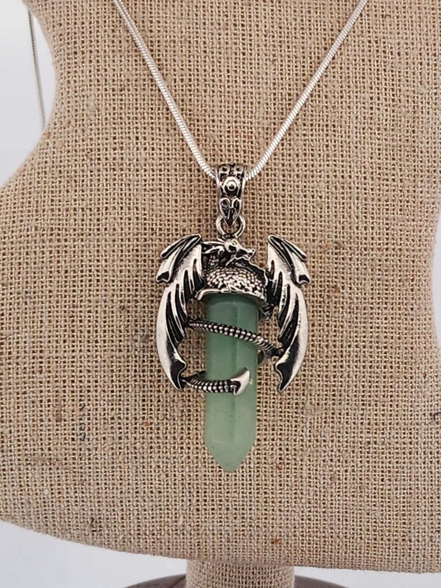 Necklace with a green pendant and silver dragon design on a beige stand.