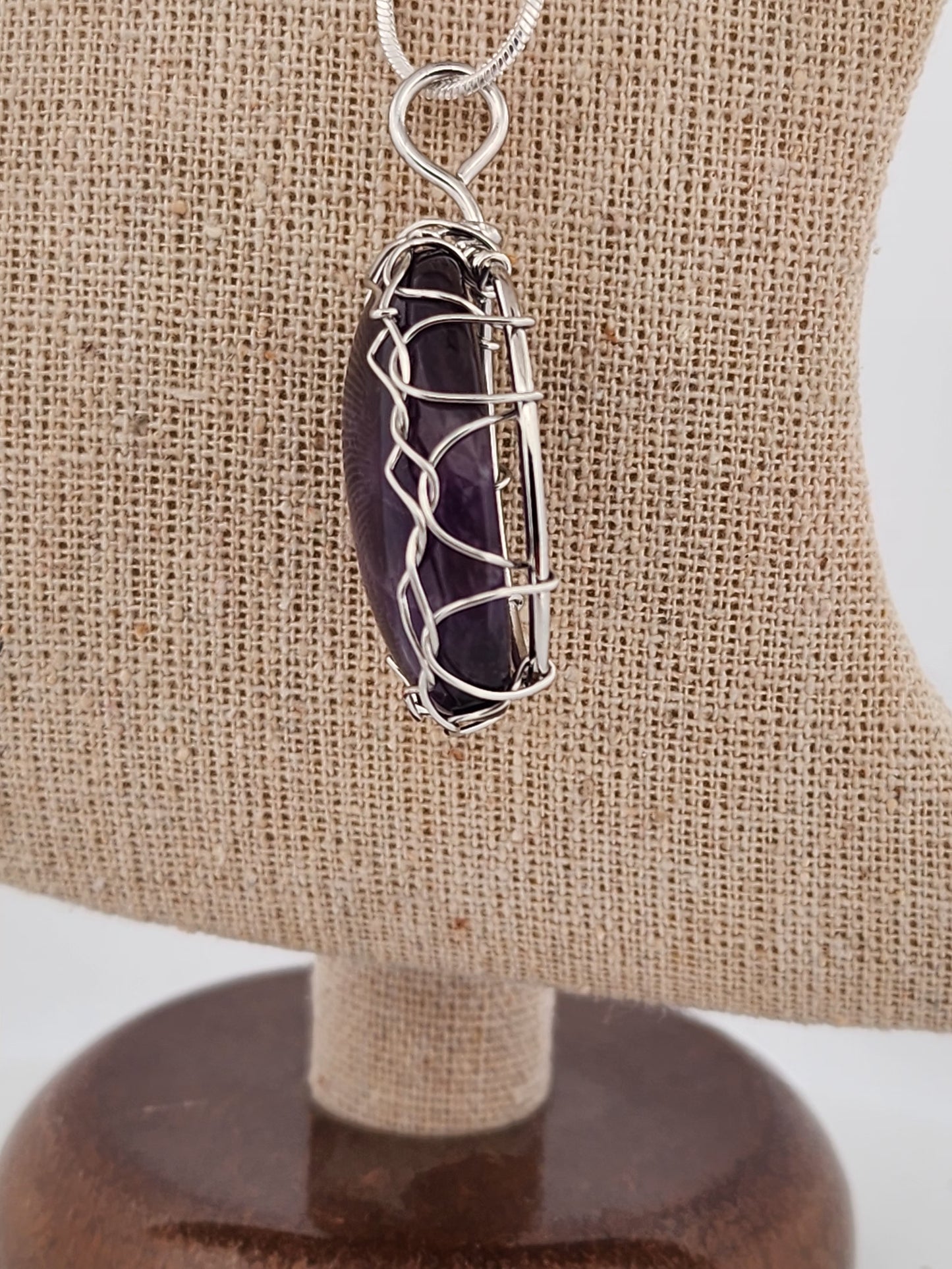 Amethyst crystal pendant with silver wire wrapping on a beige stand