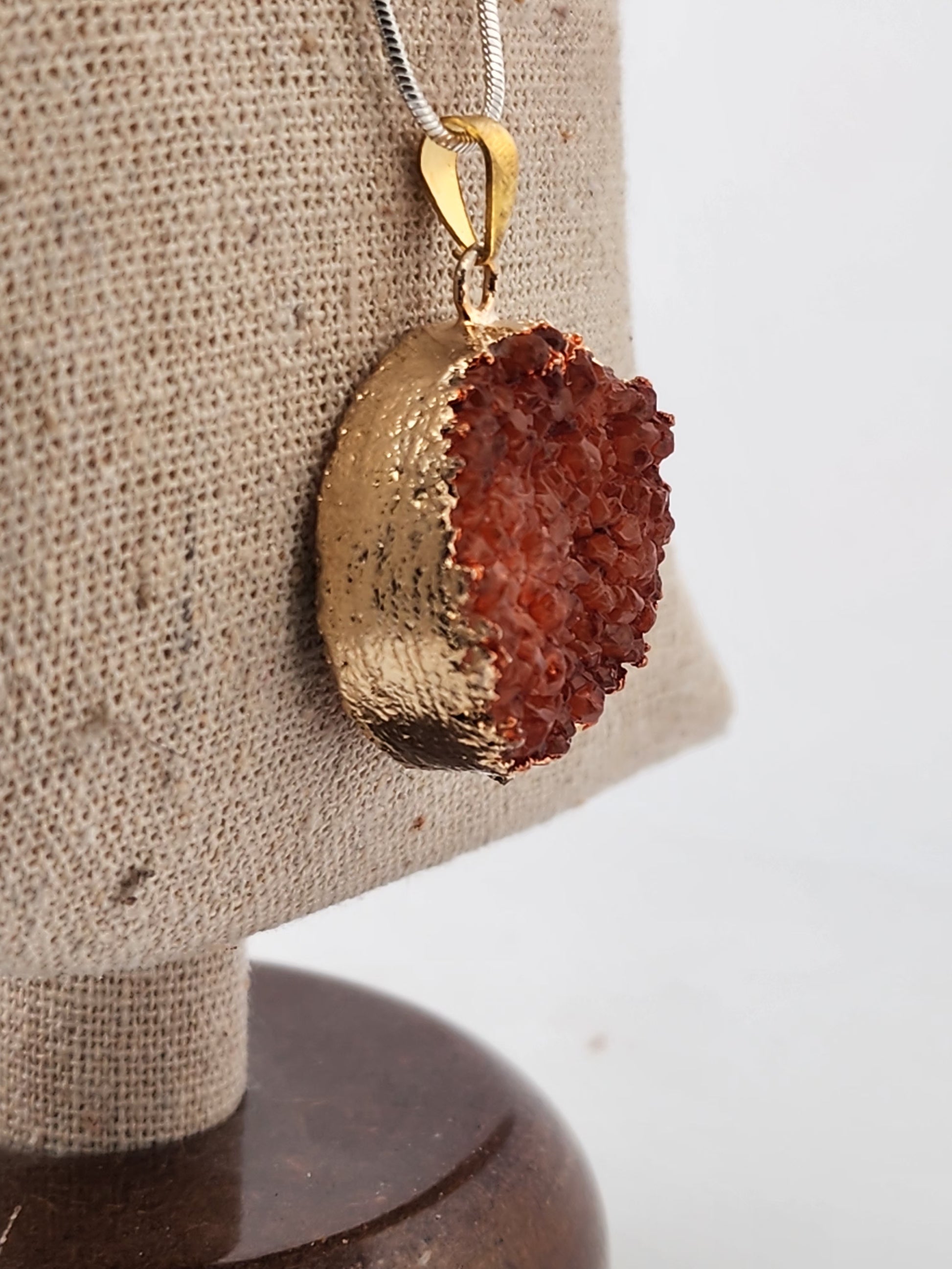 Gold pendant with a red stone on a beige stand
