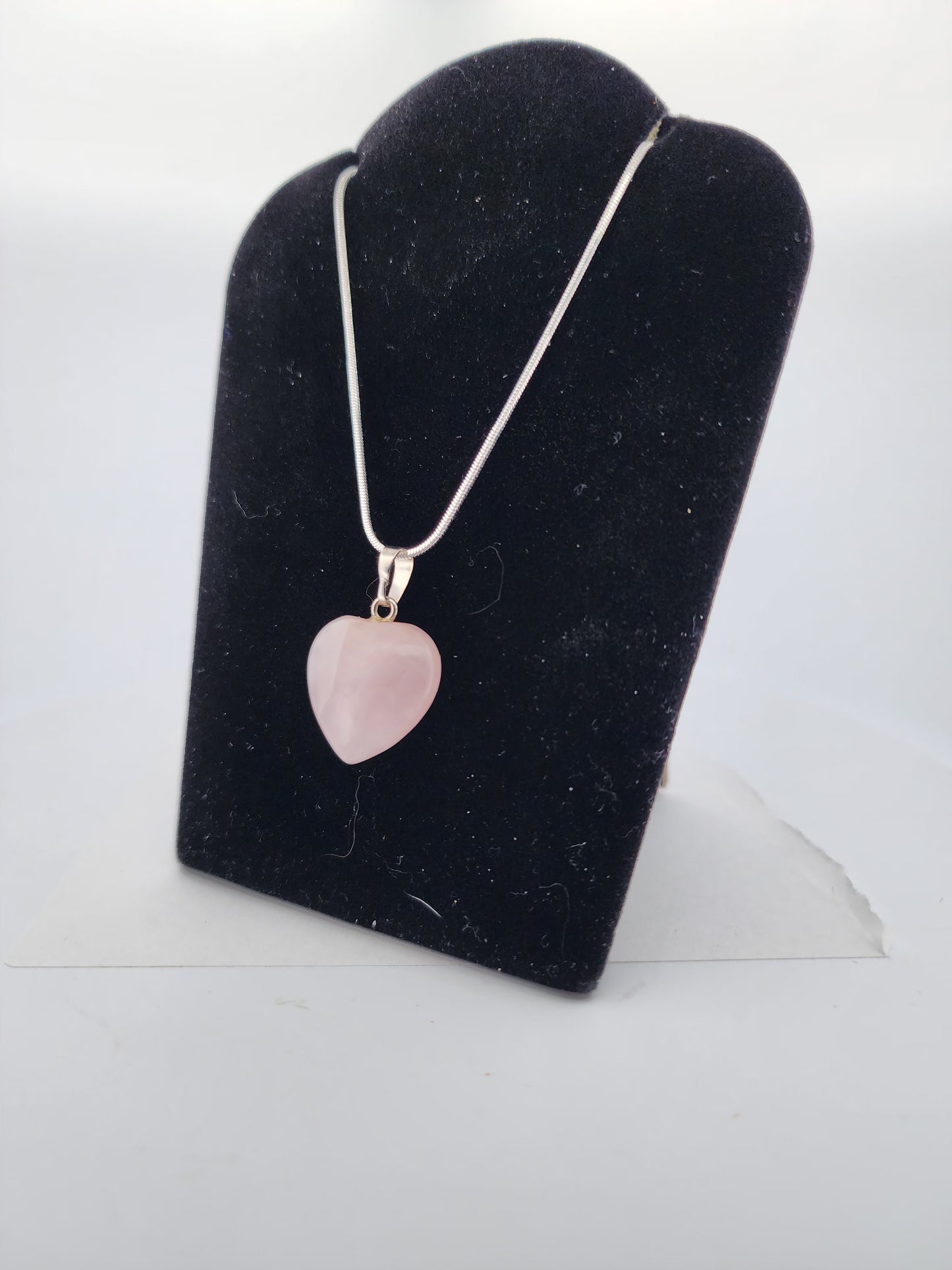 Necklace with a pink heart-shaped pendant on a black stand against a white background