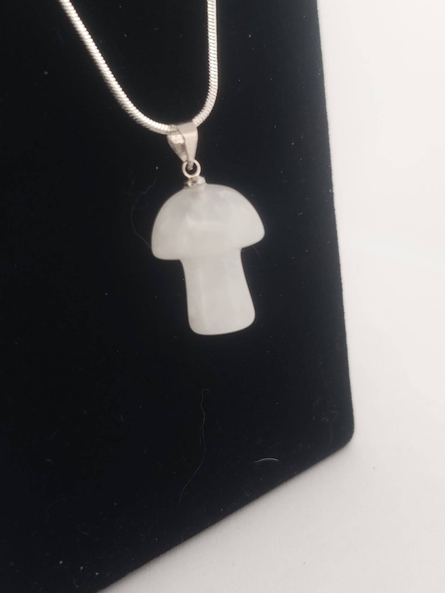 White stone pendant on a chain against a black background