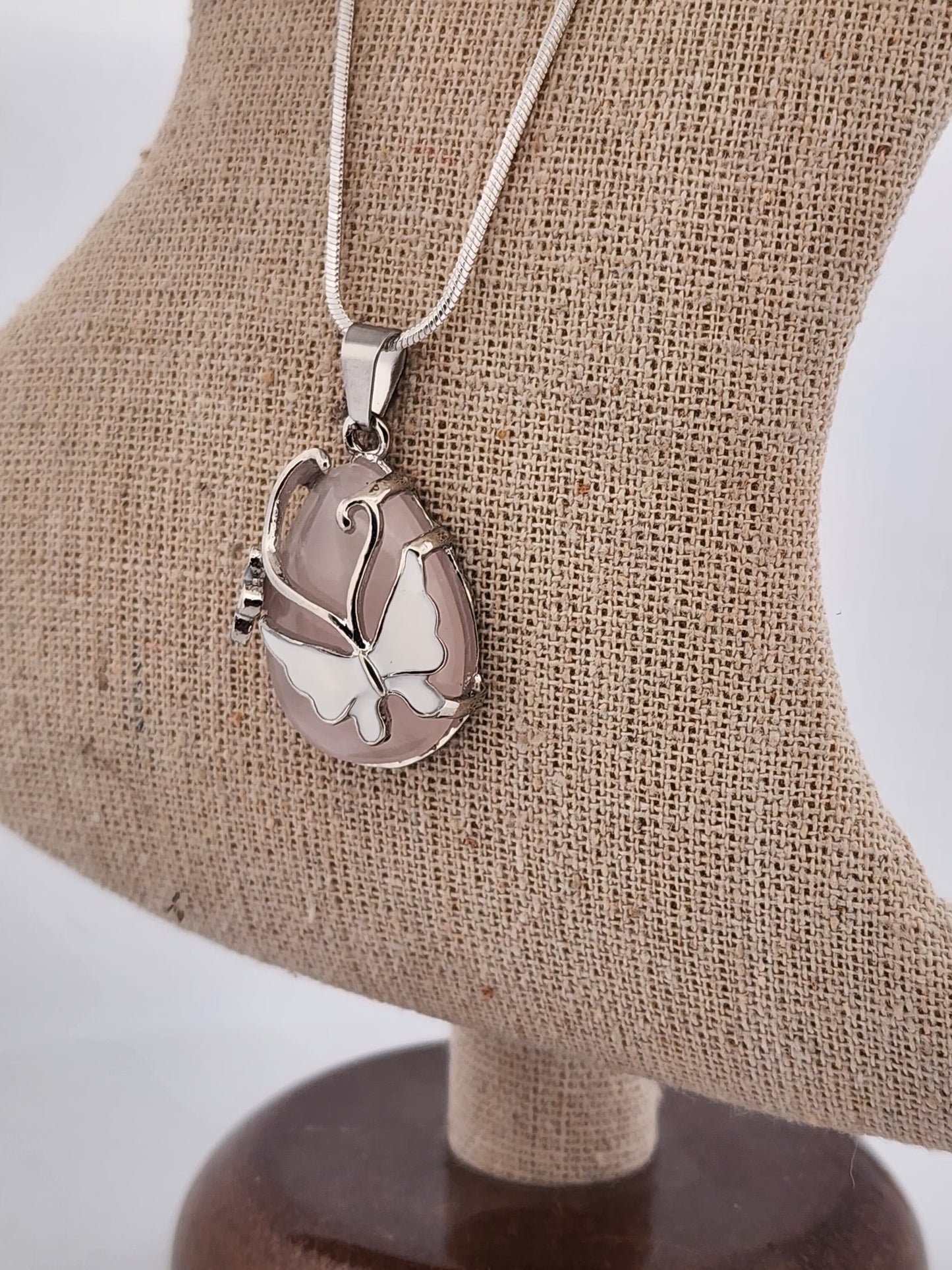 Silver butterfly pendant necklace on a brown textured stand with a white background