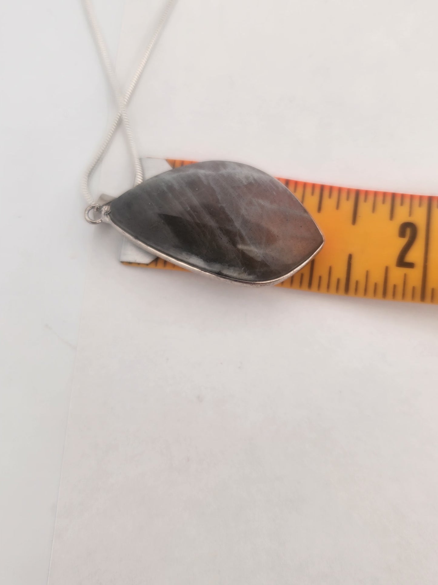 Metallic pendant on a chain with a measuring tape for scale on a white background
