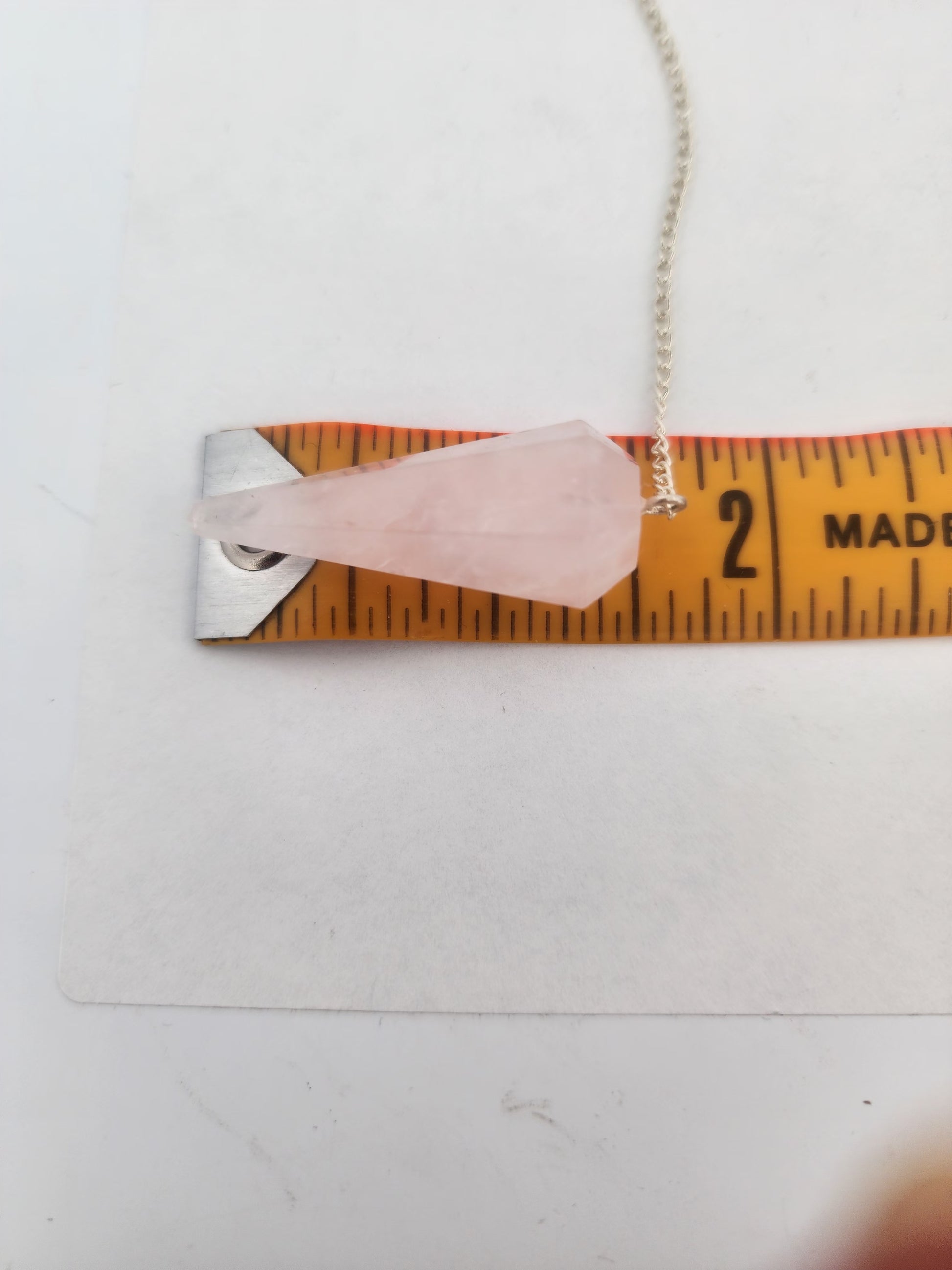 Necklace with a pink crystal pendant on a ruler for scale