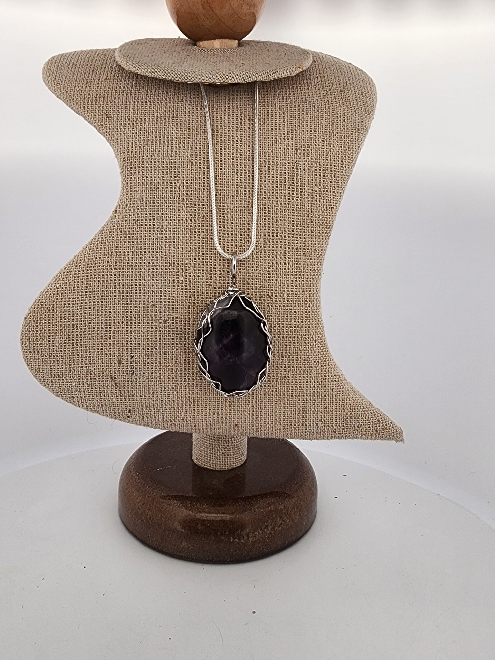 Necklace with a black pendant on a brown jewelry stand against a white background