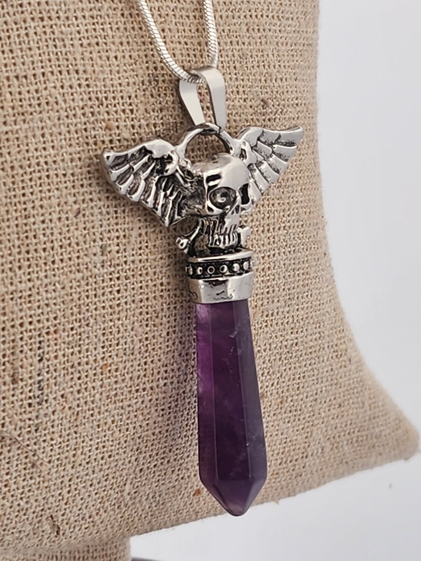 Silver pendant with eagle design and purple crystal on a beige fabric background