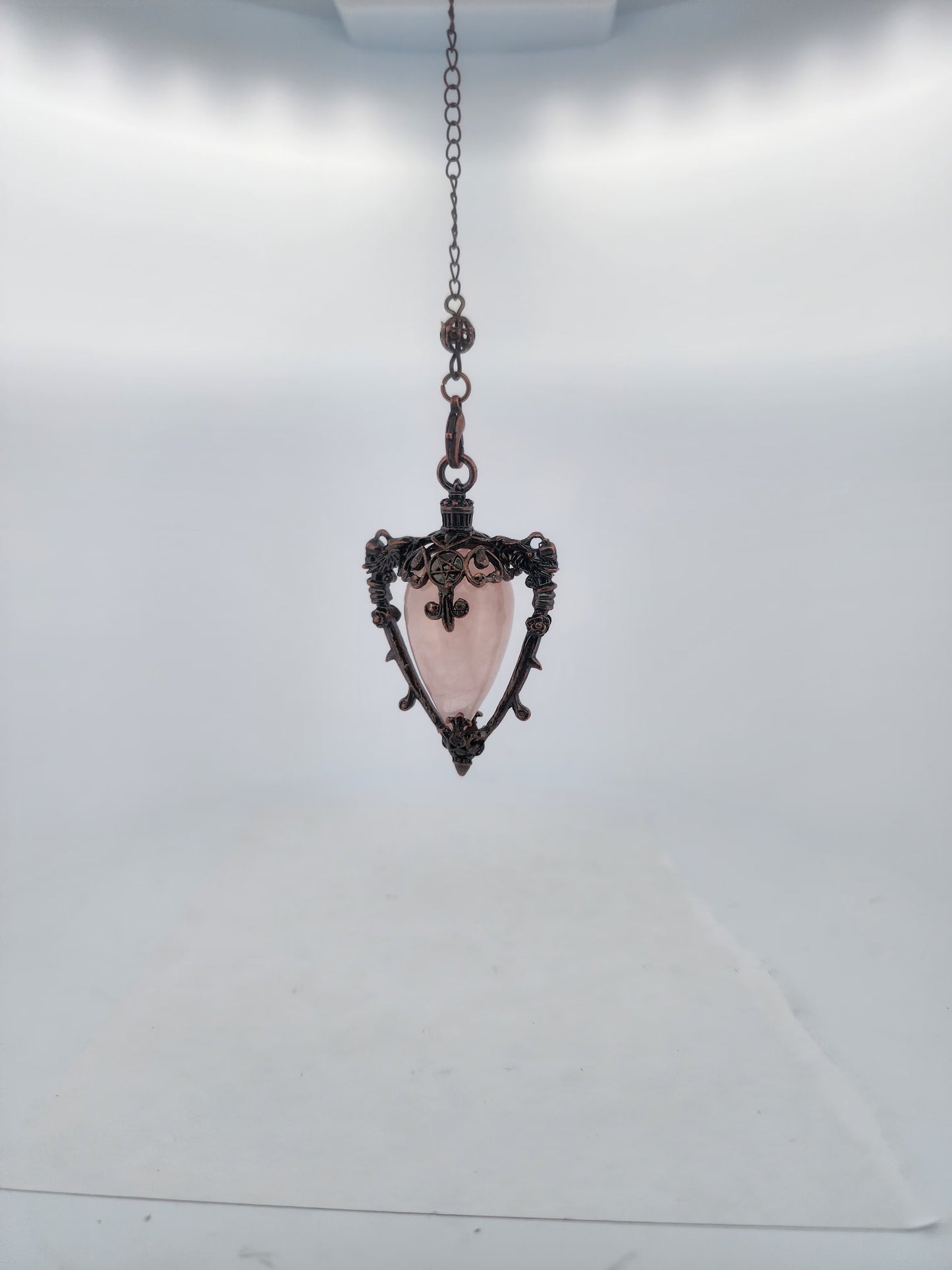 Decorative pendant with pink central stone and intricate metalwork on a white background