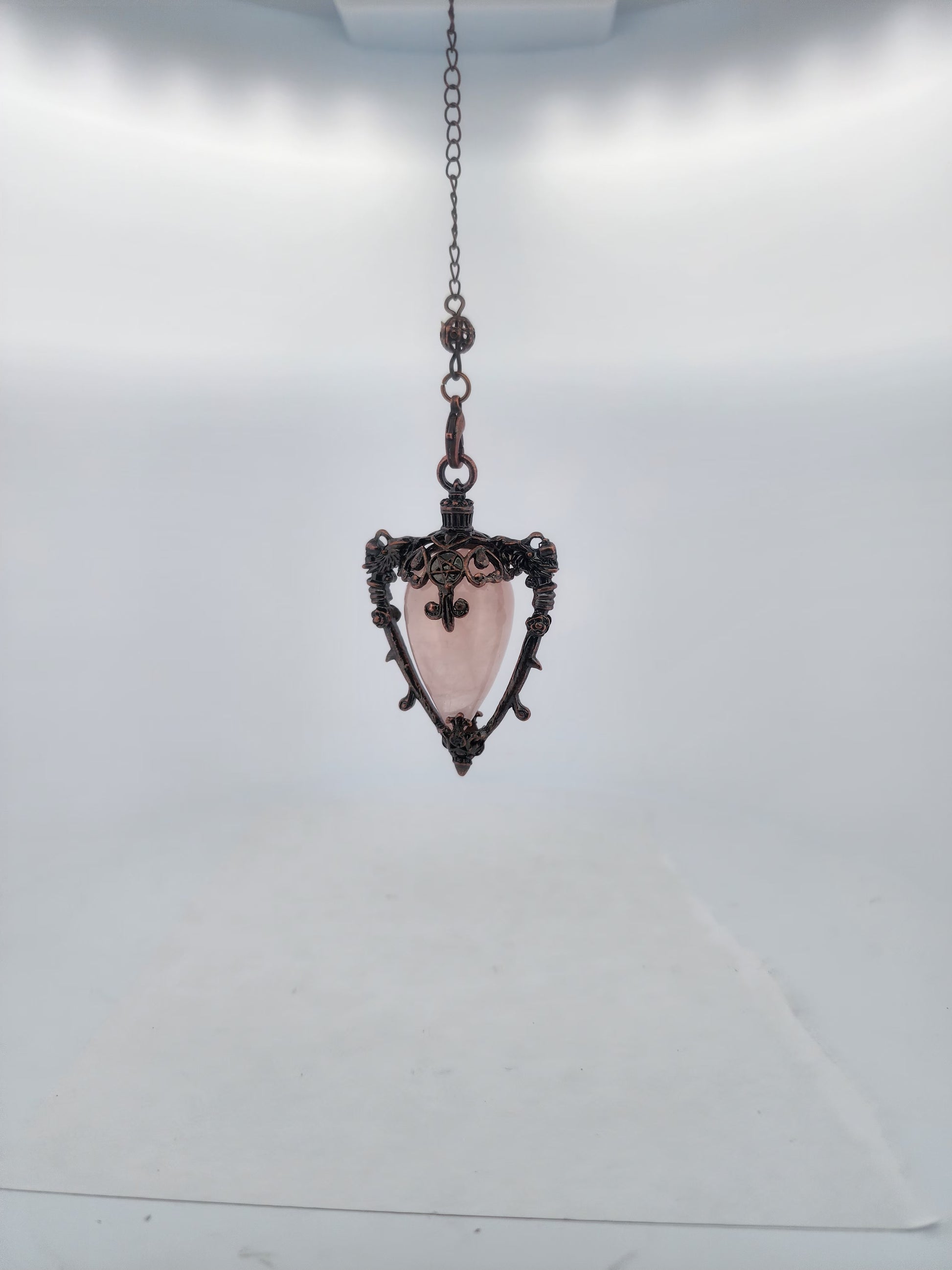 Decorative pendant with pink central stone and intricate metalwork on a white background