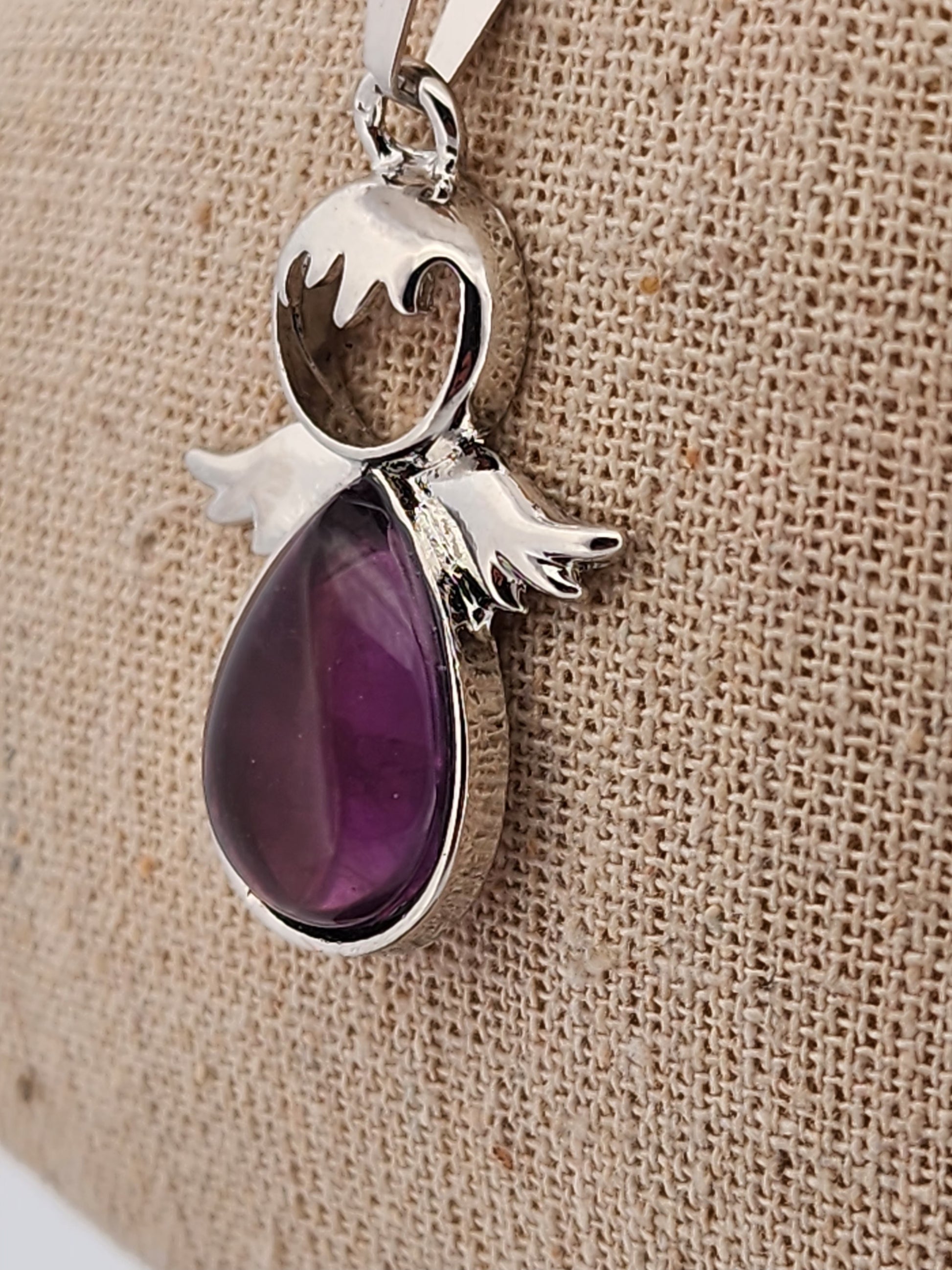 Silver pendant with a purple gemstone on a beige fabric background