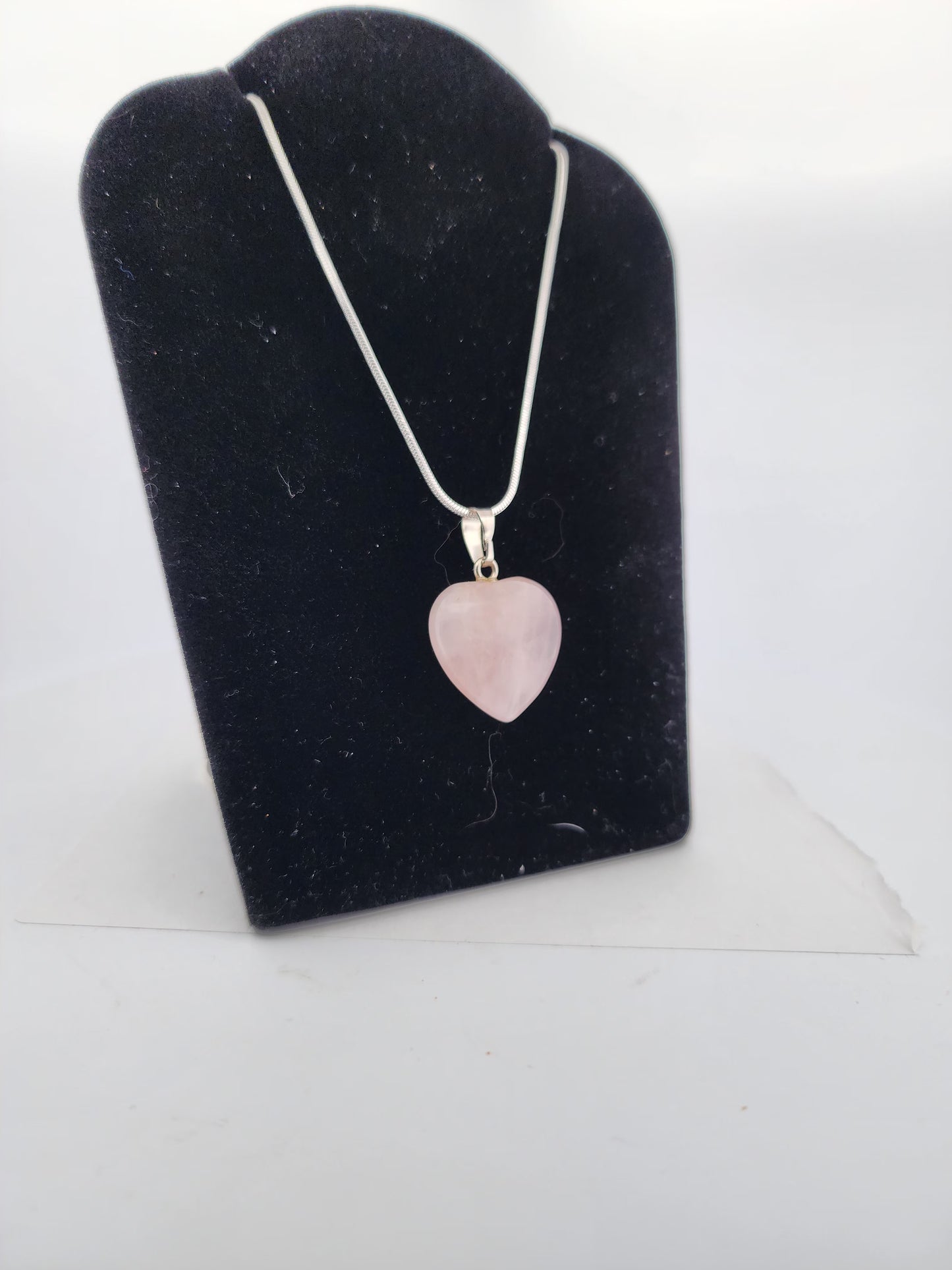 Necklace with a heart-shaped pink pendant on a black stand against a white background