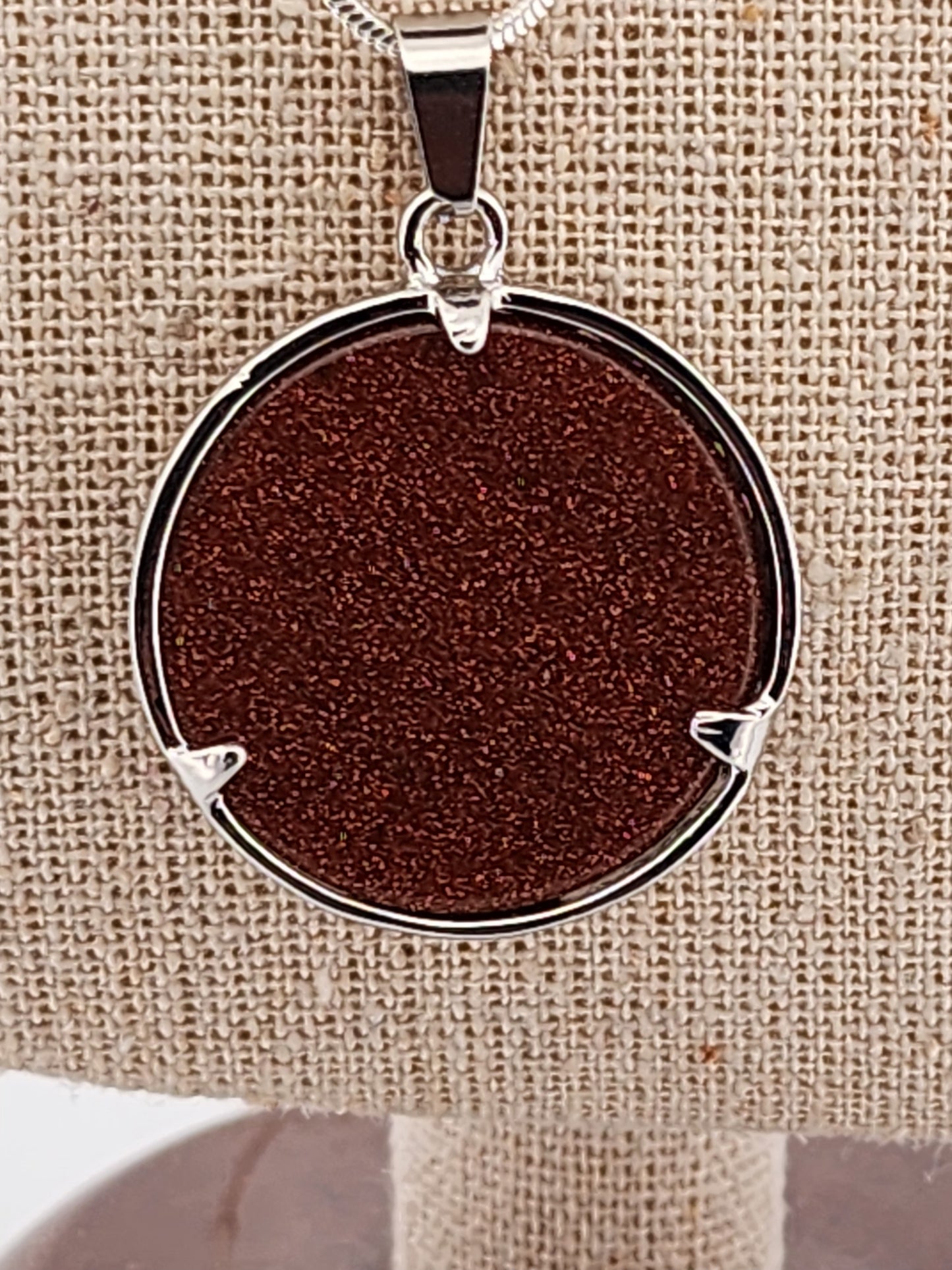 Round pendant with brown center and silver frame on a beige fabric background