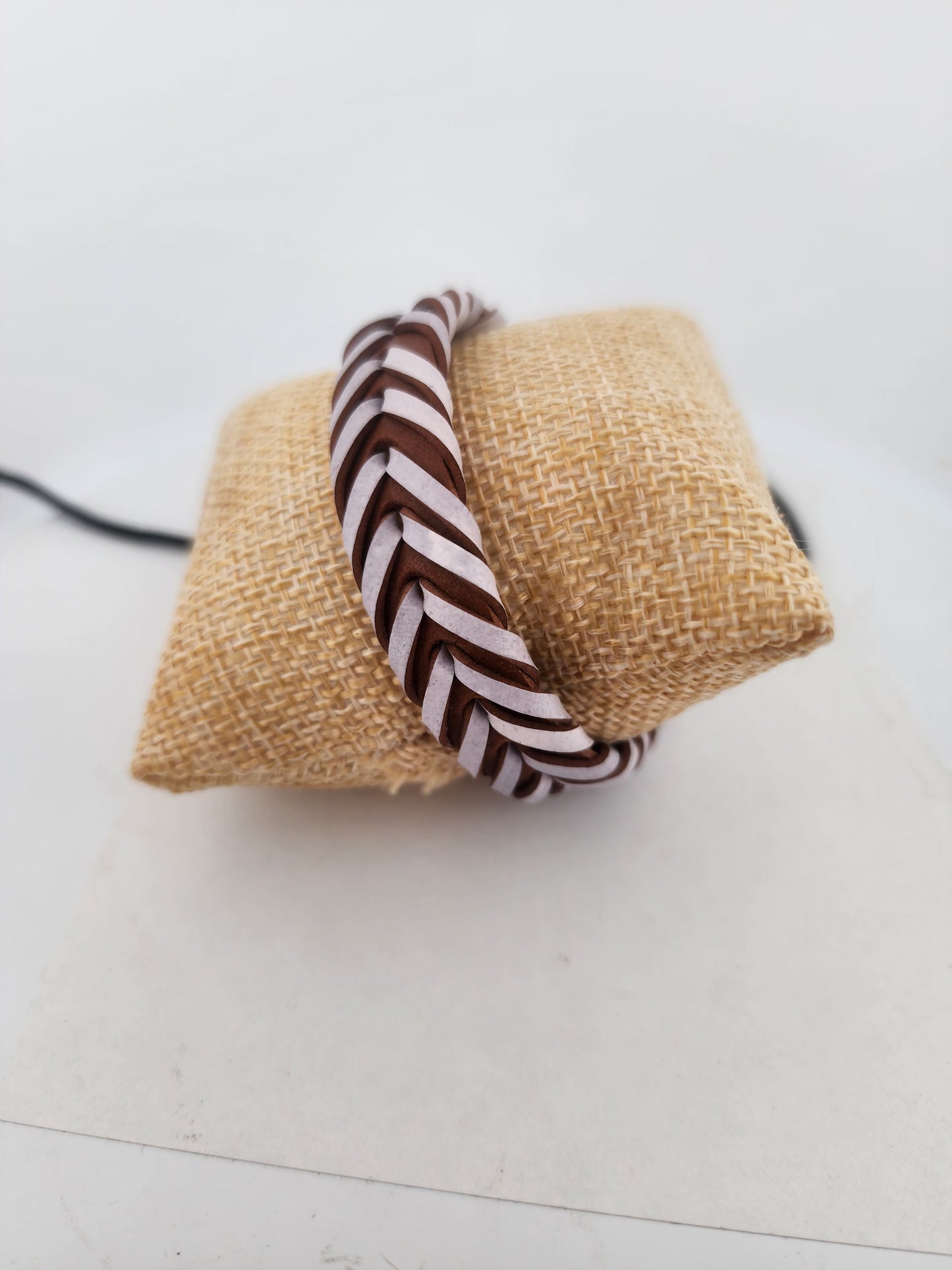 Braided brown and white hairband on a textured beige square