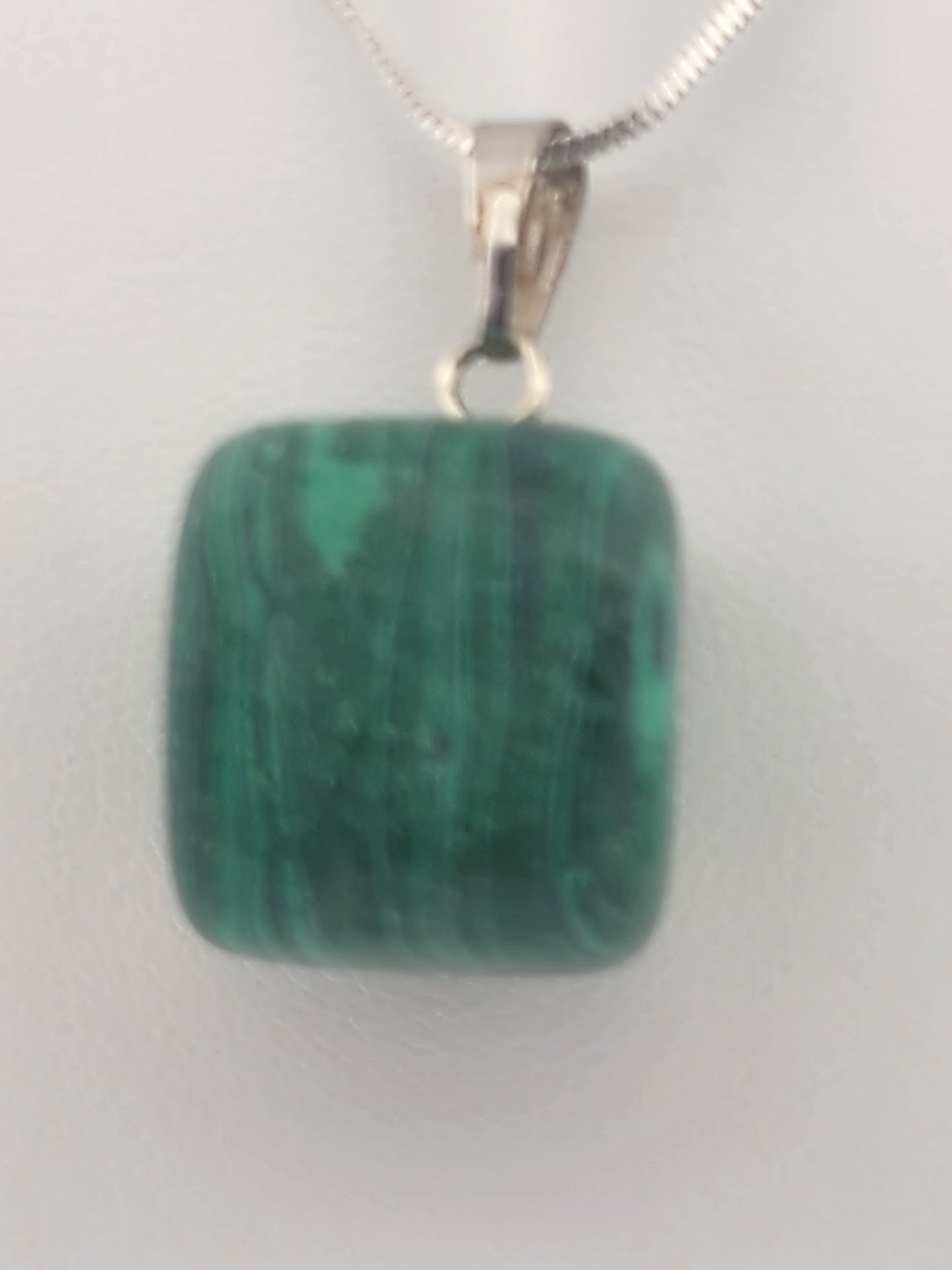 Green malachite pendant on a silver chain against a white background
