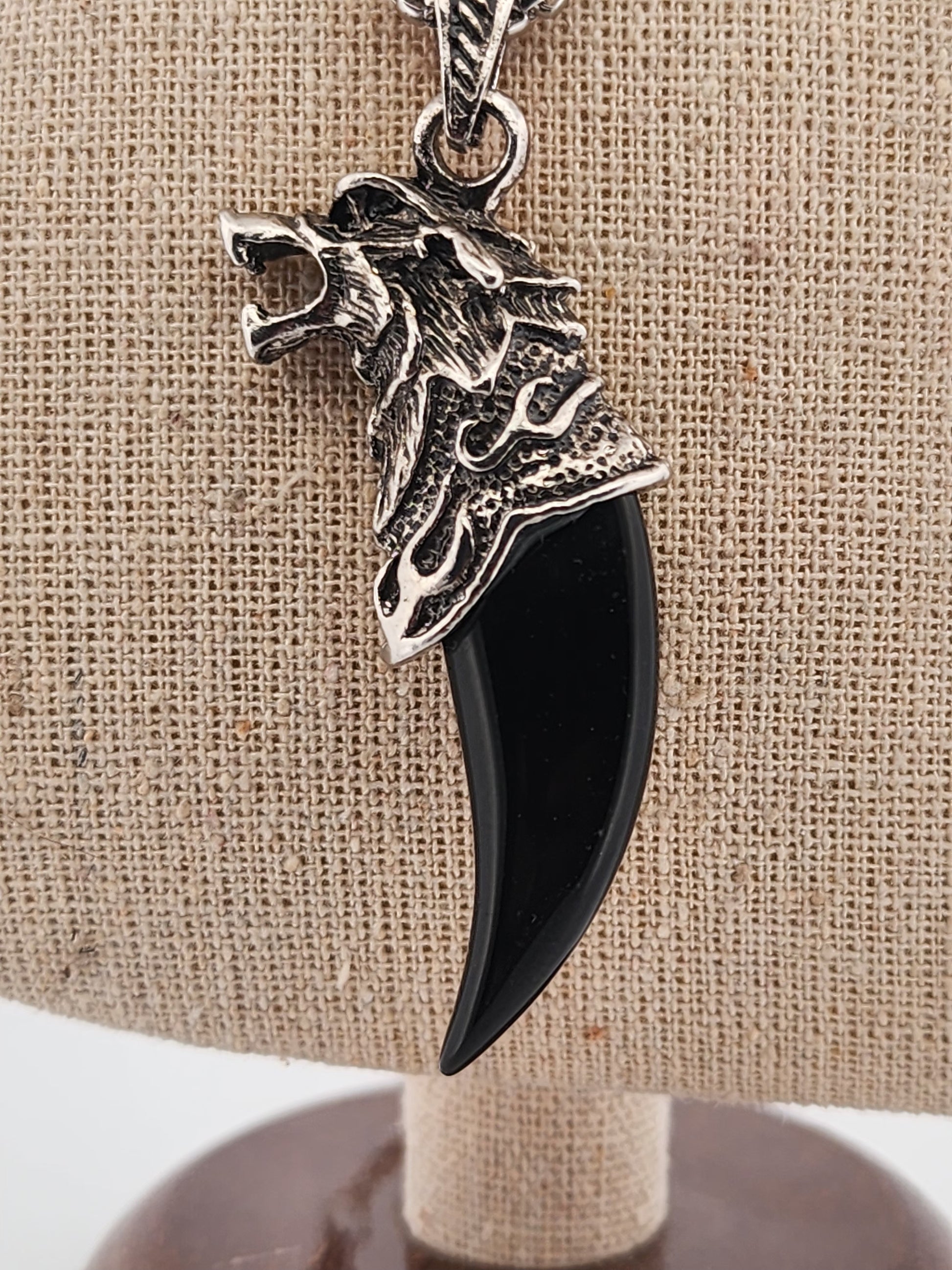 Pendant with black claw and silver wolf head on a beige background