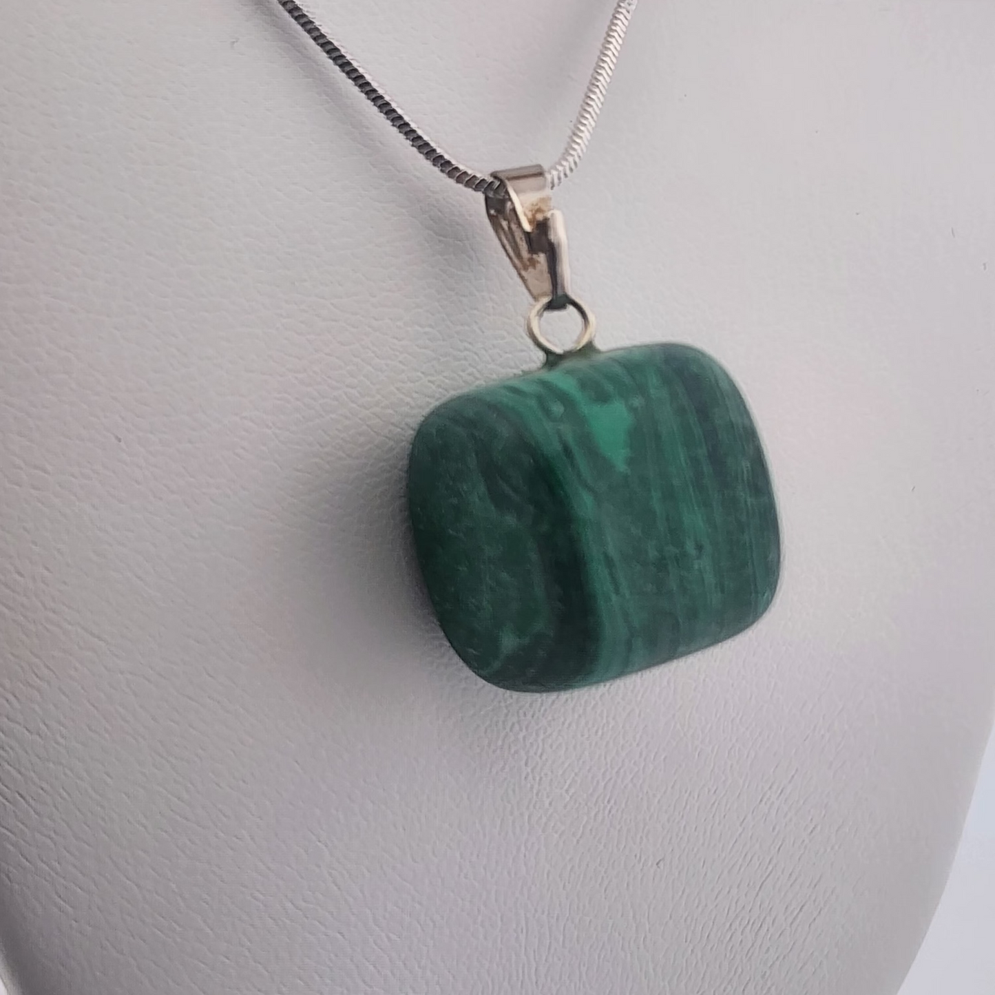 Green stone pendant on a silver chain against a gray background