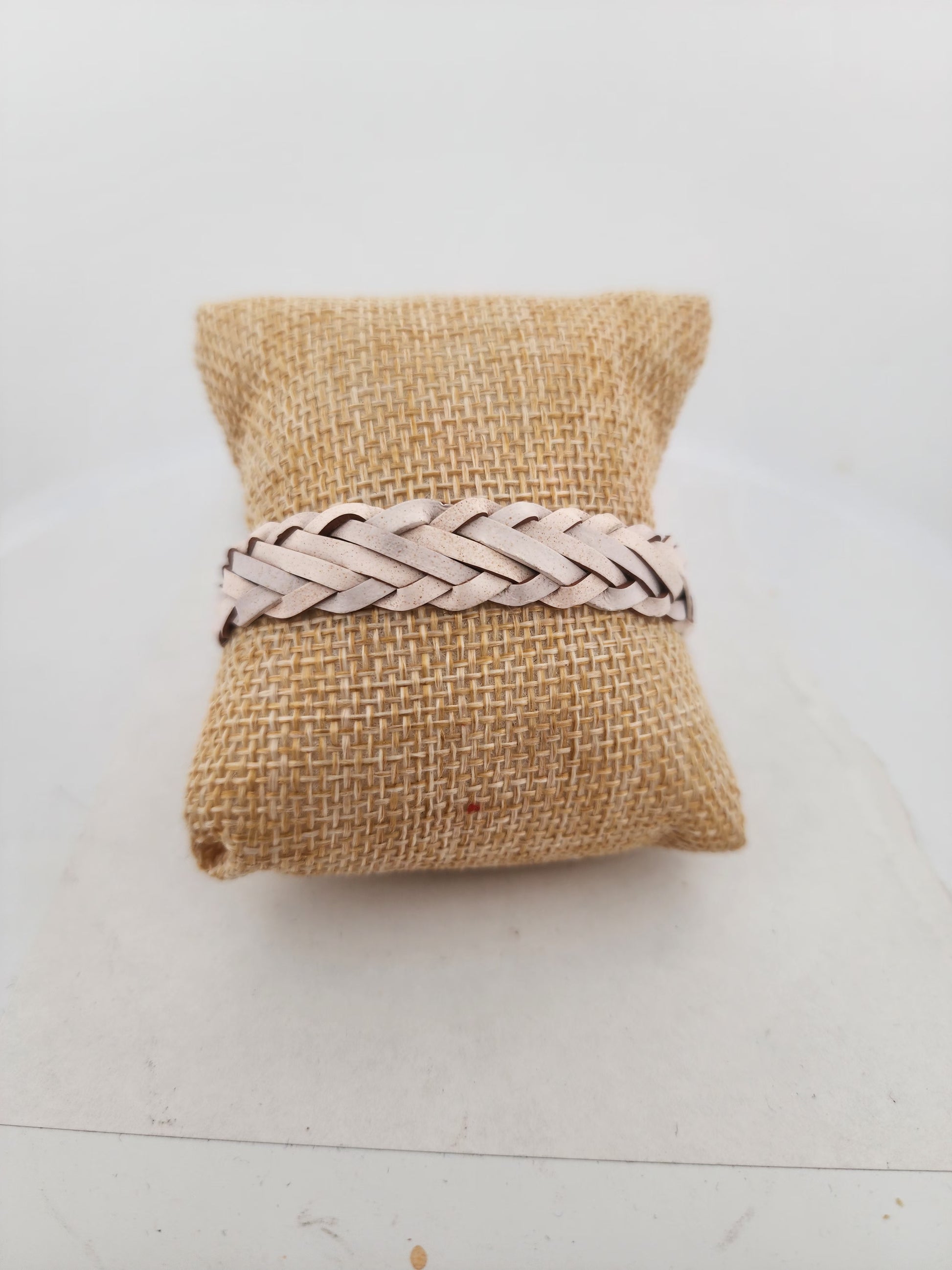 Braided leather bracelet on a burlap pillow against a white background