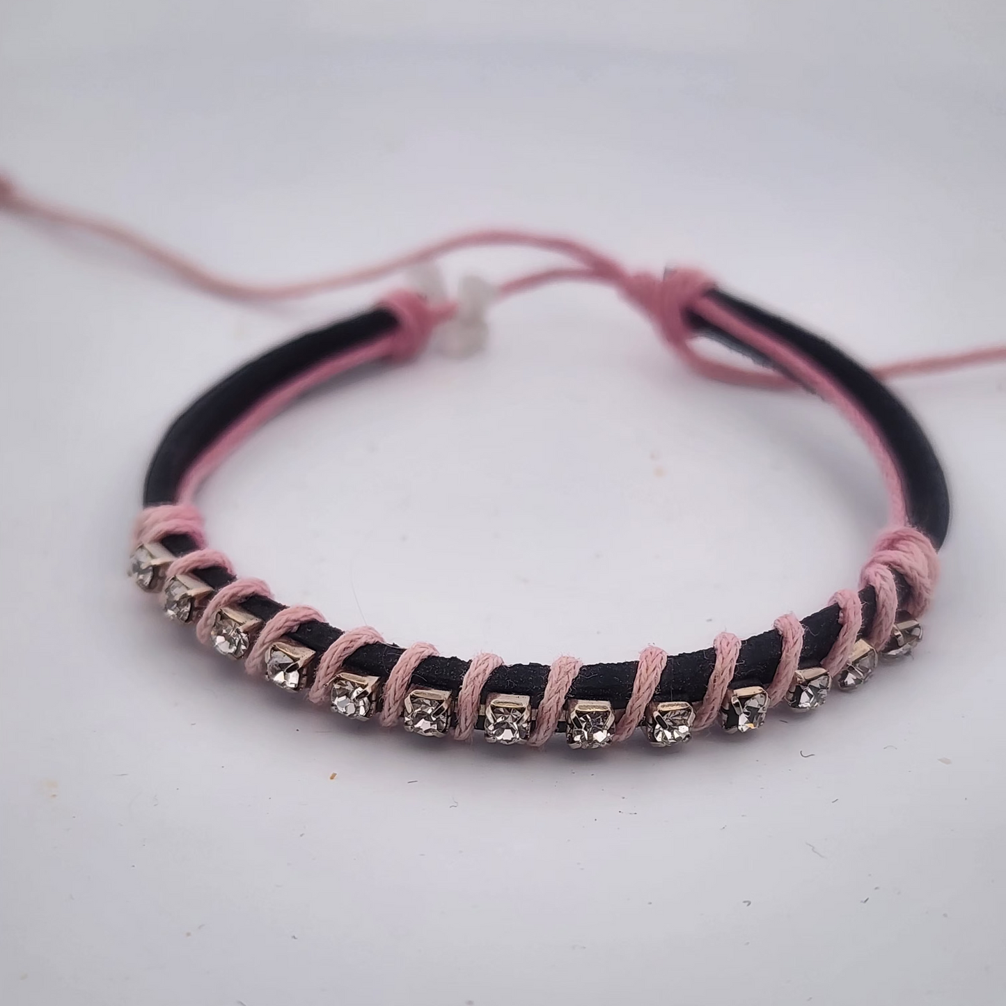 Bracelet with pink and black cord and embedded stones on a white background