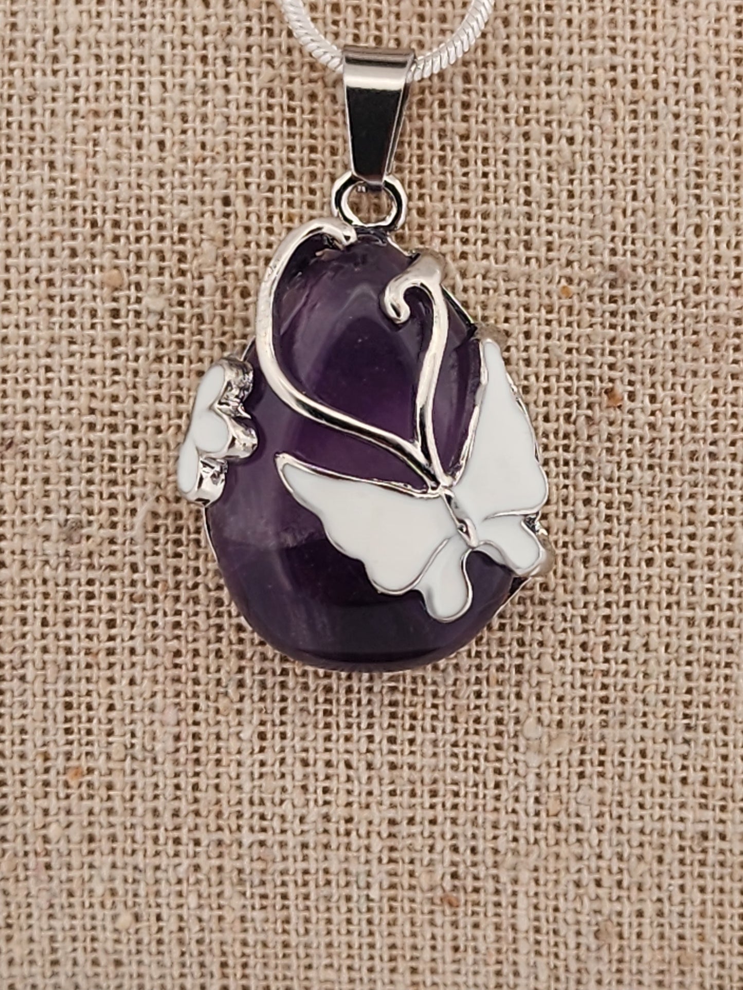 Purple pendant with silver butterfly design on a beige fabric background