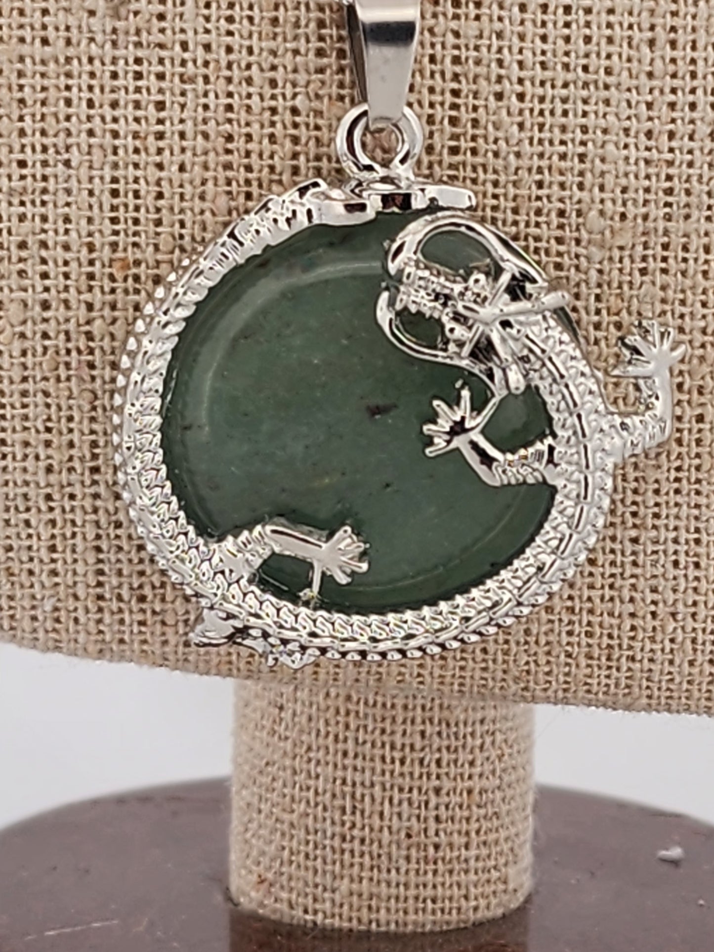 Silver pendant with green stone on a beige stand