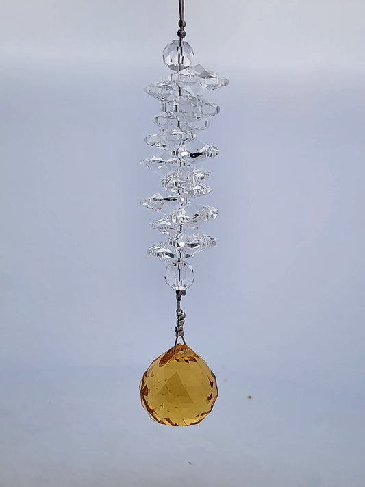 Crystal hanging ornament with a yellow gemstone against a gray background