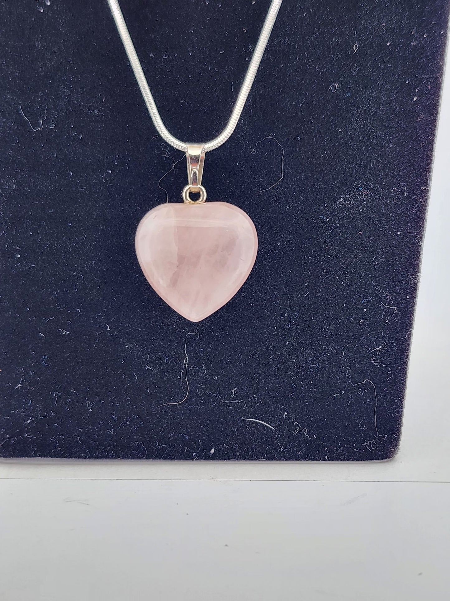 Pink heart-shaped pendant on a silver chain against a dark blue background