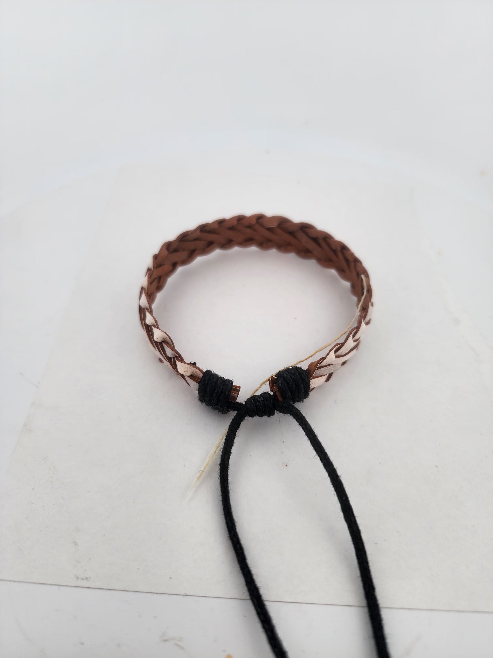 Brown braided bracelet with black cord on a white background