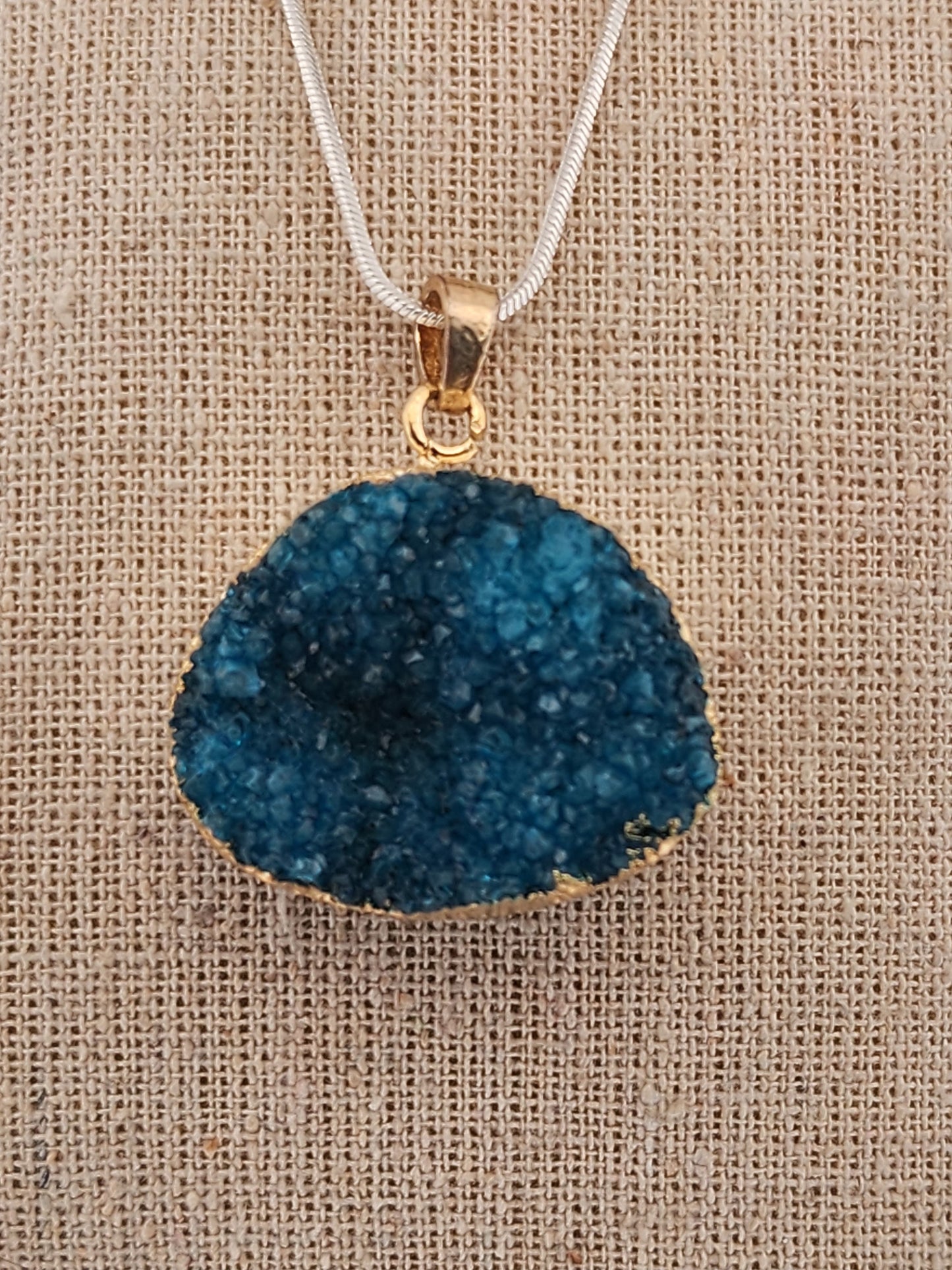 Blue druzy pendant necklace on a beige fabric background