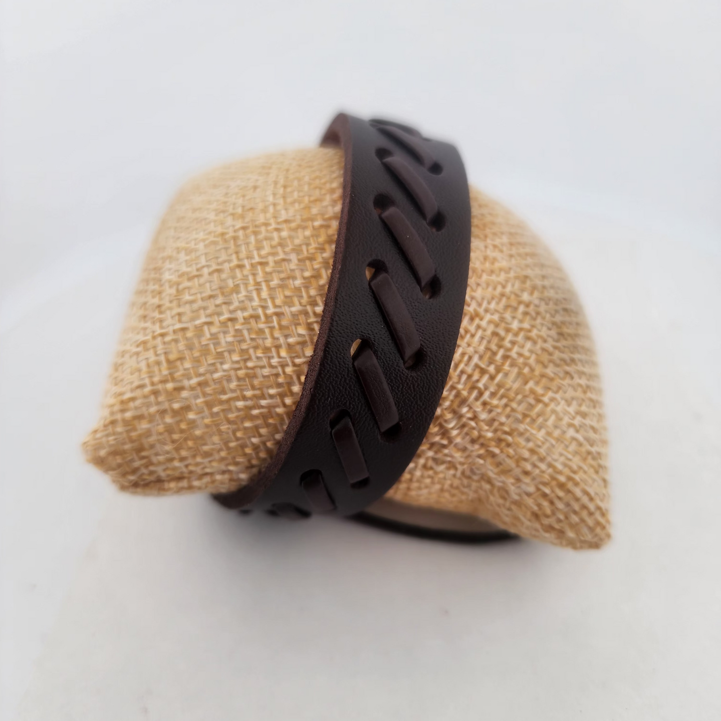Brown bracelet on a textured beige stand against a white background