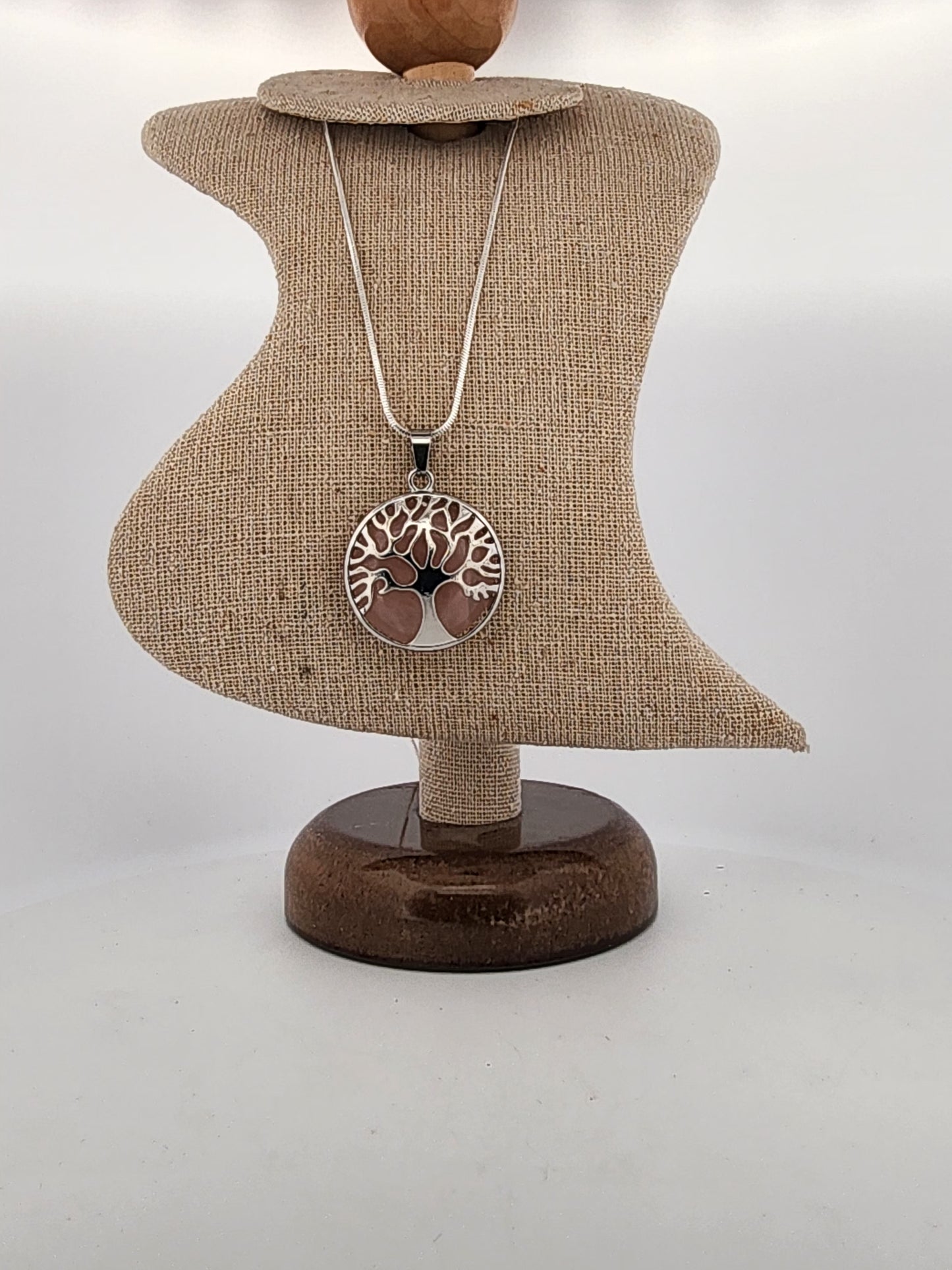 Necklace with a tree of life pendant on a brown jewelry stand against a white background