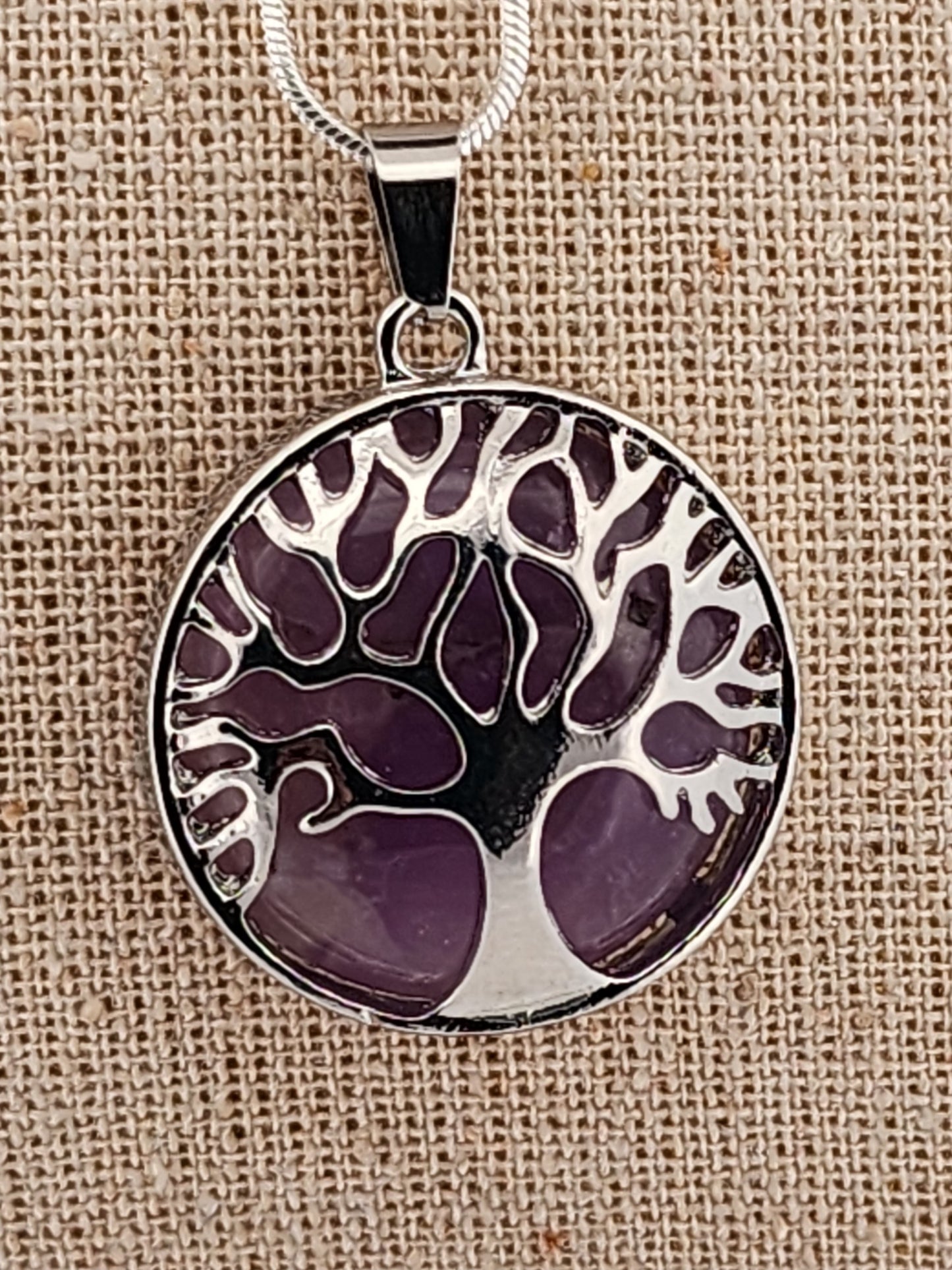 Tree of life pendant with purple design on a beige fabric background