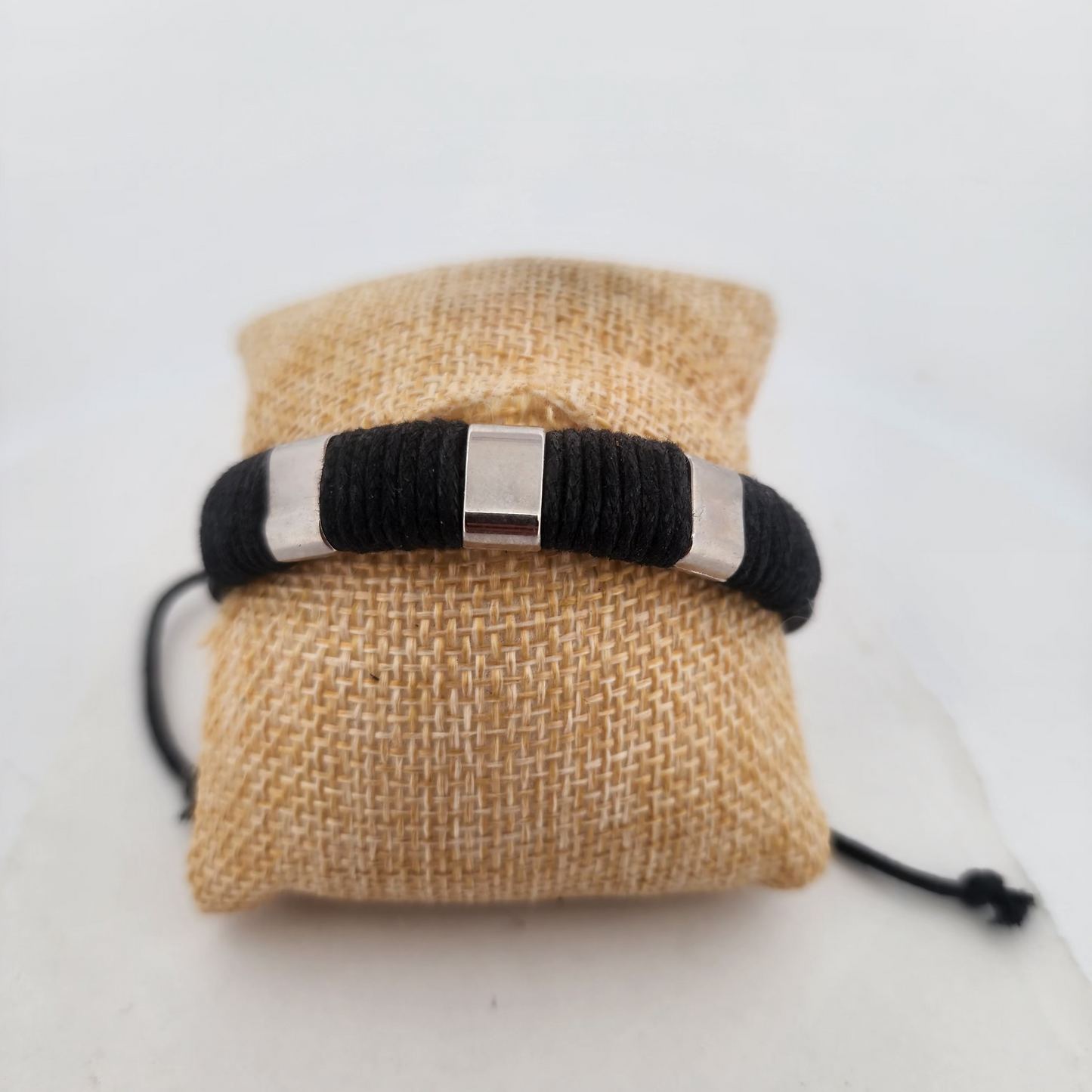 Black braided bracelet with silver clasp on a beige drawstring bag against a white background