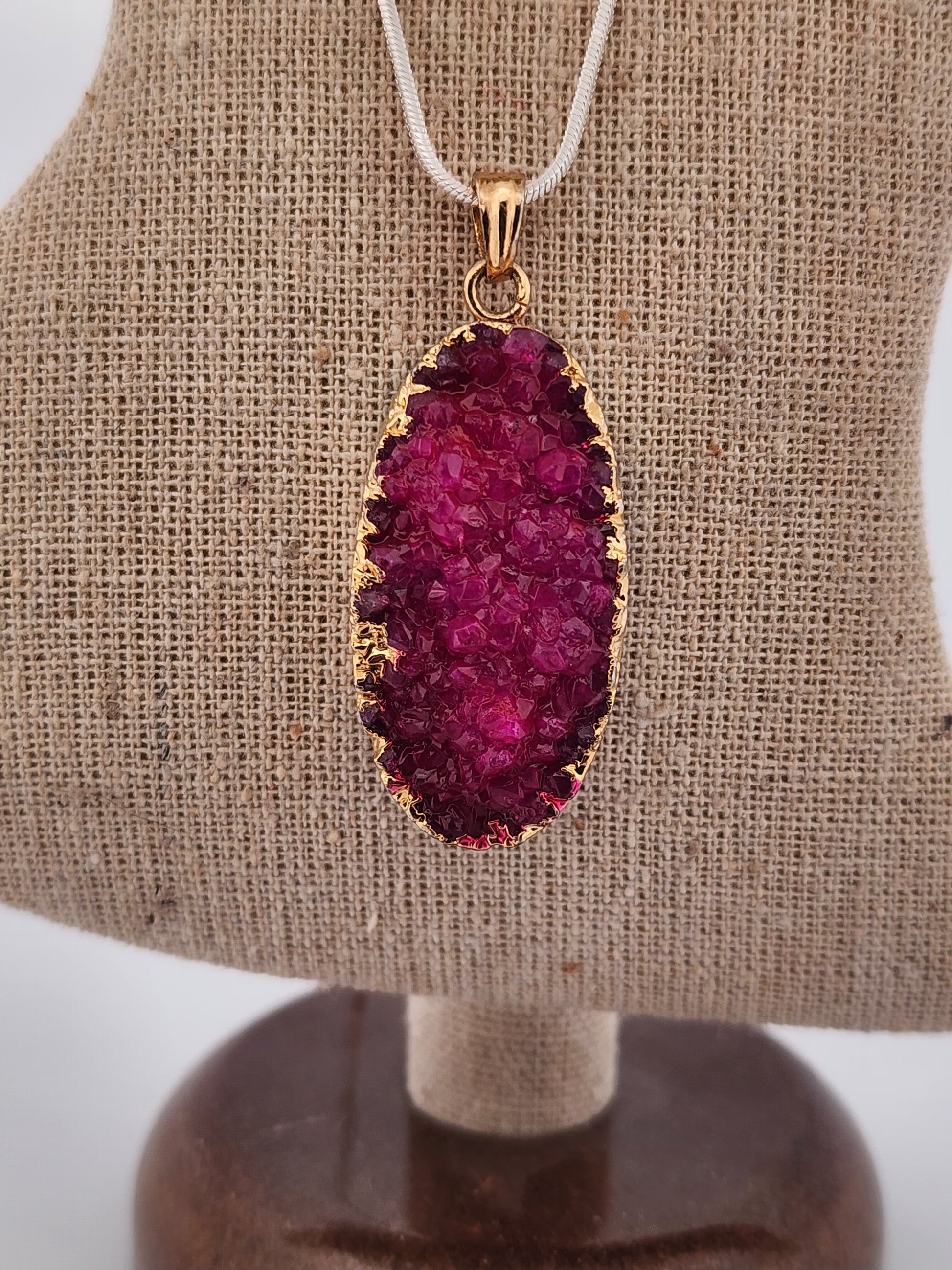 Purple druzy pendant with gold trim on a beige display stand.