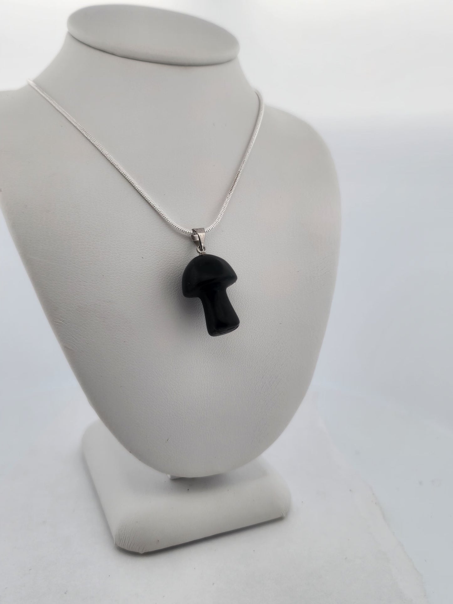 Black mushroom pendant on a silver chain displayed on a gray bust