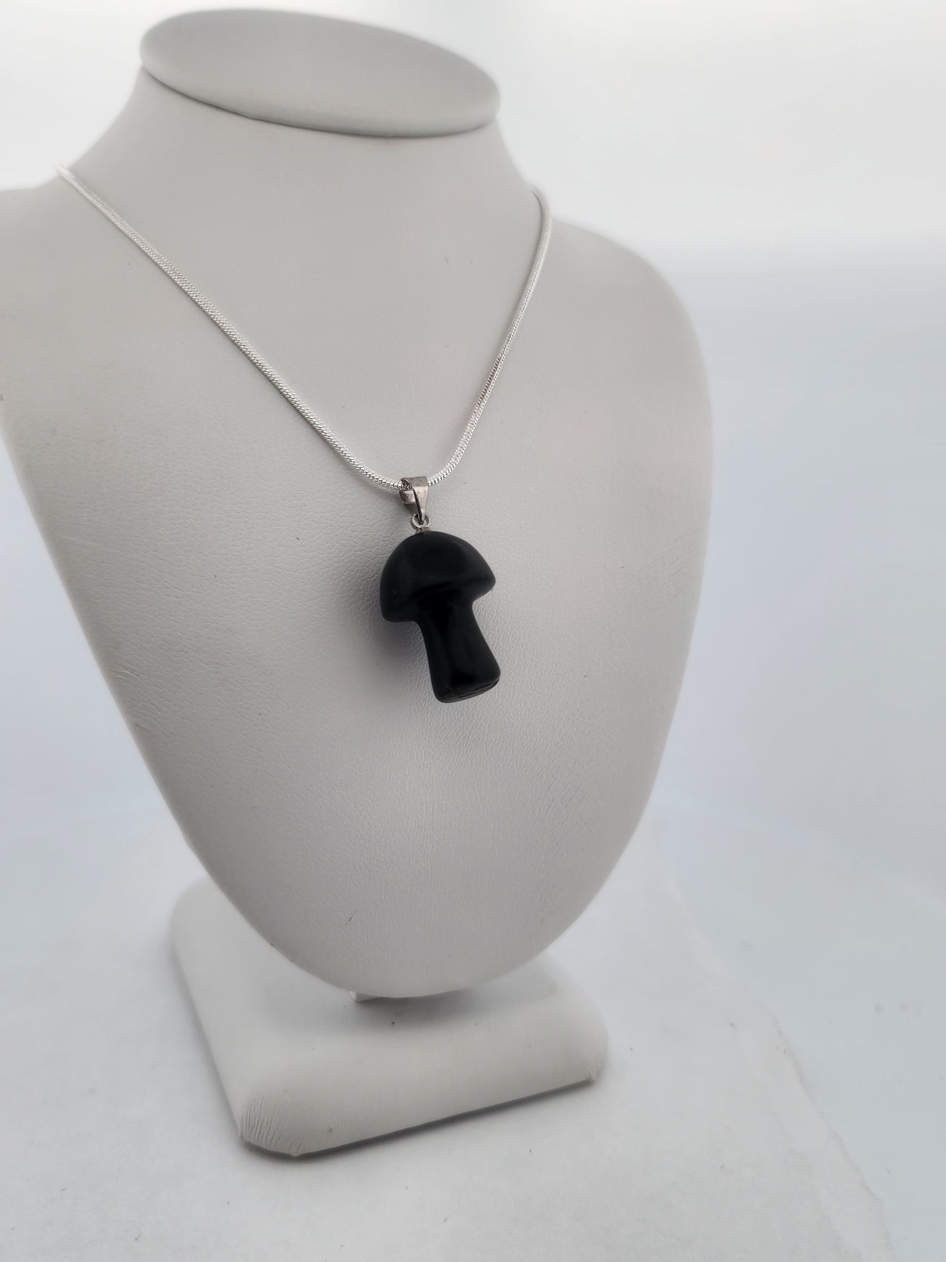 Black mushroom pendant on a silver chain displayed on a gray bust